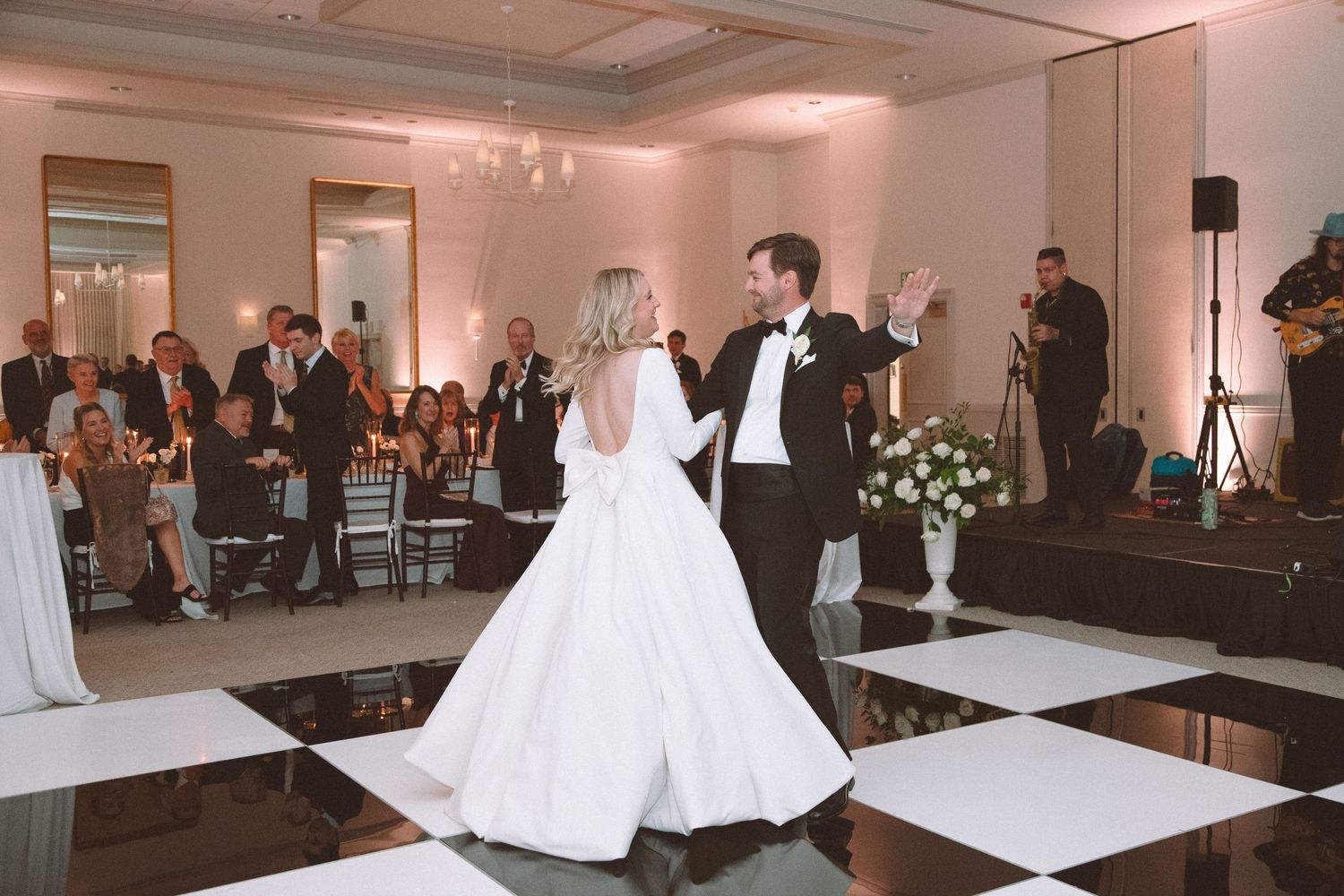 Bride and groom sharing first dance on black and white checkered floor at elegant reception.
