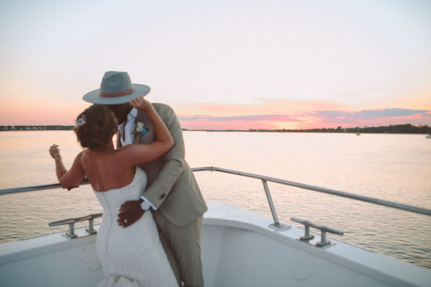 A bride and groom share a joyful embrace on a yacht bow against a stunning pink sunset sky.