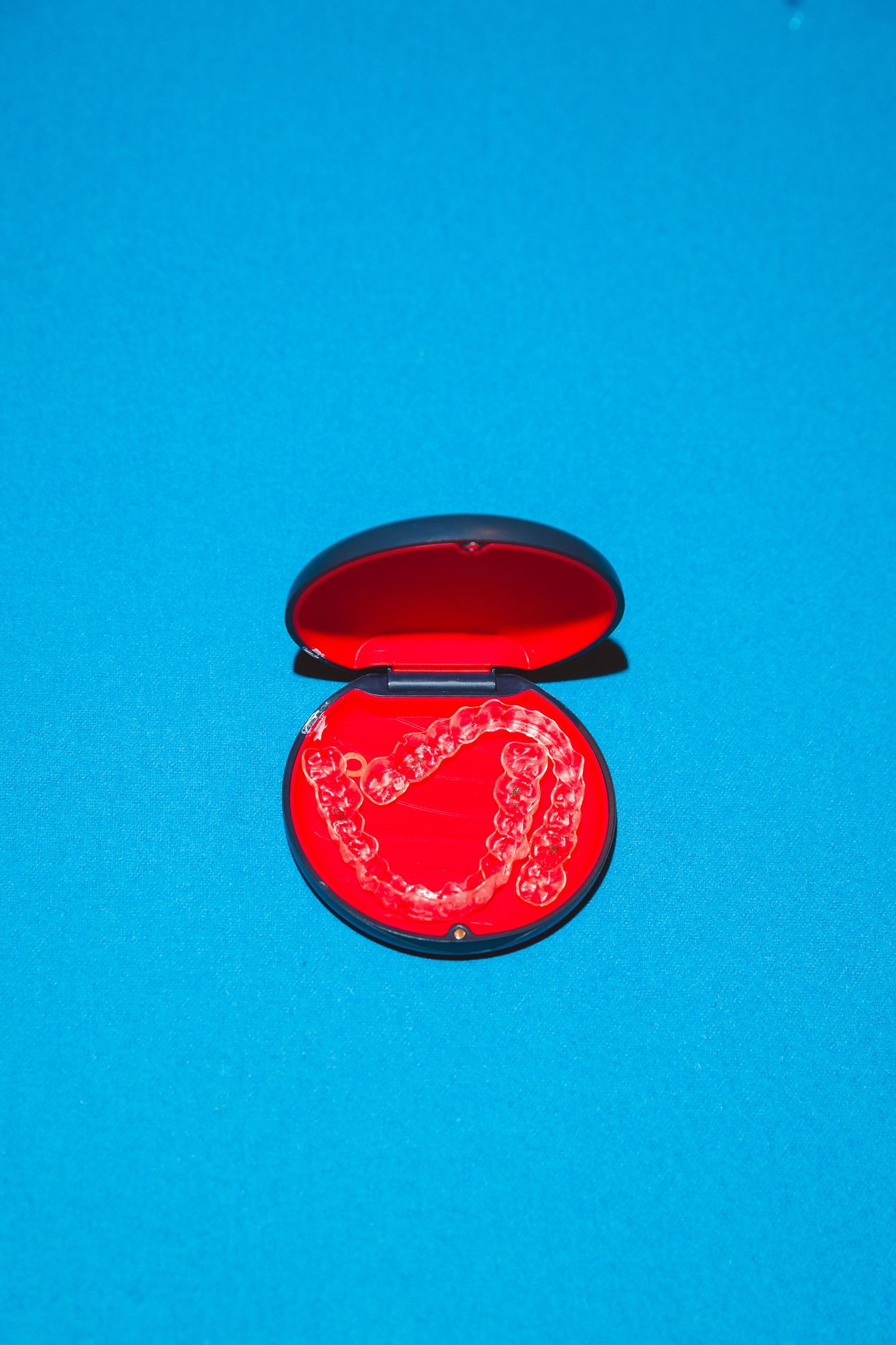 Clear dental retainer in open red-lined black case on bright blue background.