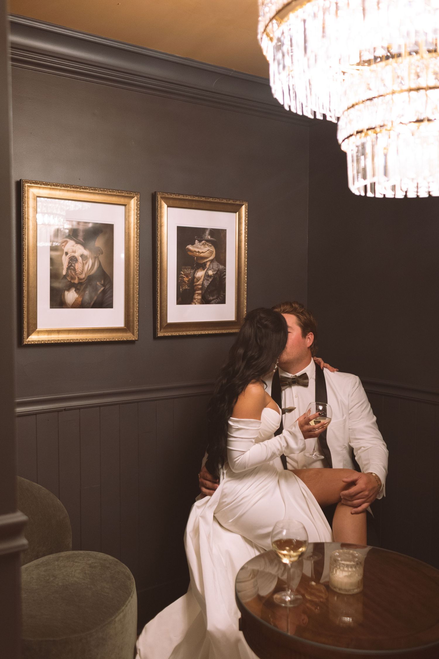 Bride and groom sharing a kiss while seated at a table in a moody, elegant lounge.