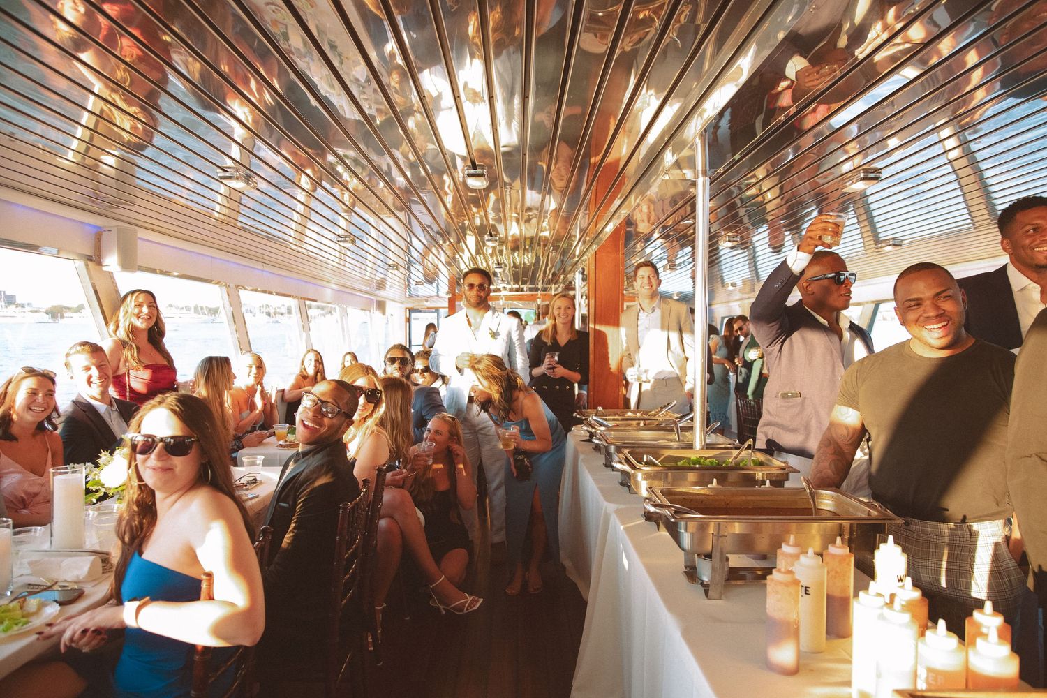 Wedding guests enjoying a buffet dinner reception aboard a decorated boat with candlelit tables.