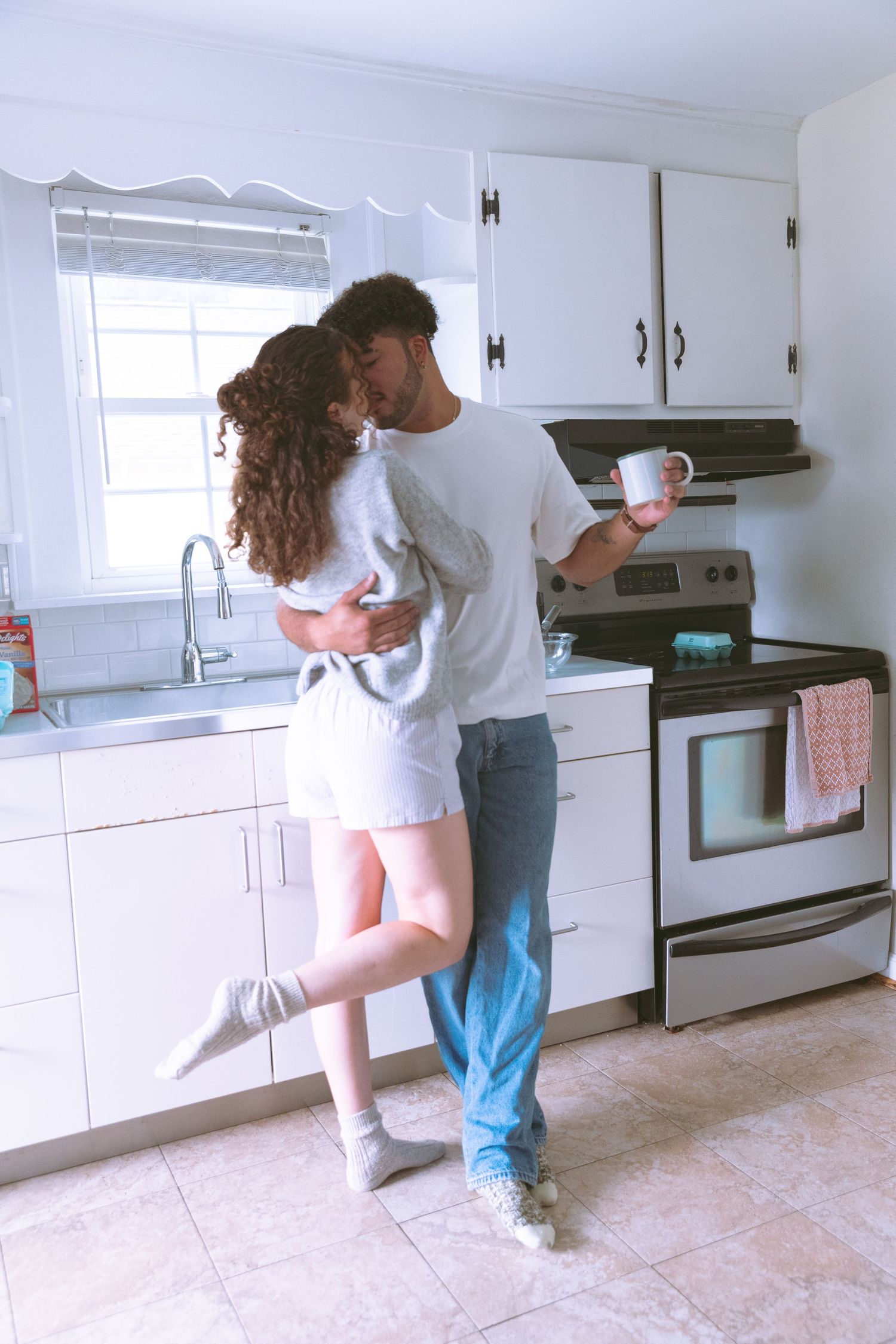 Young couple embracing and kissing in a bright white kitchen.