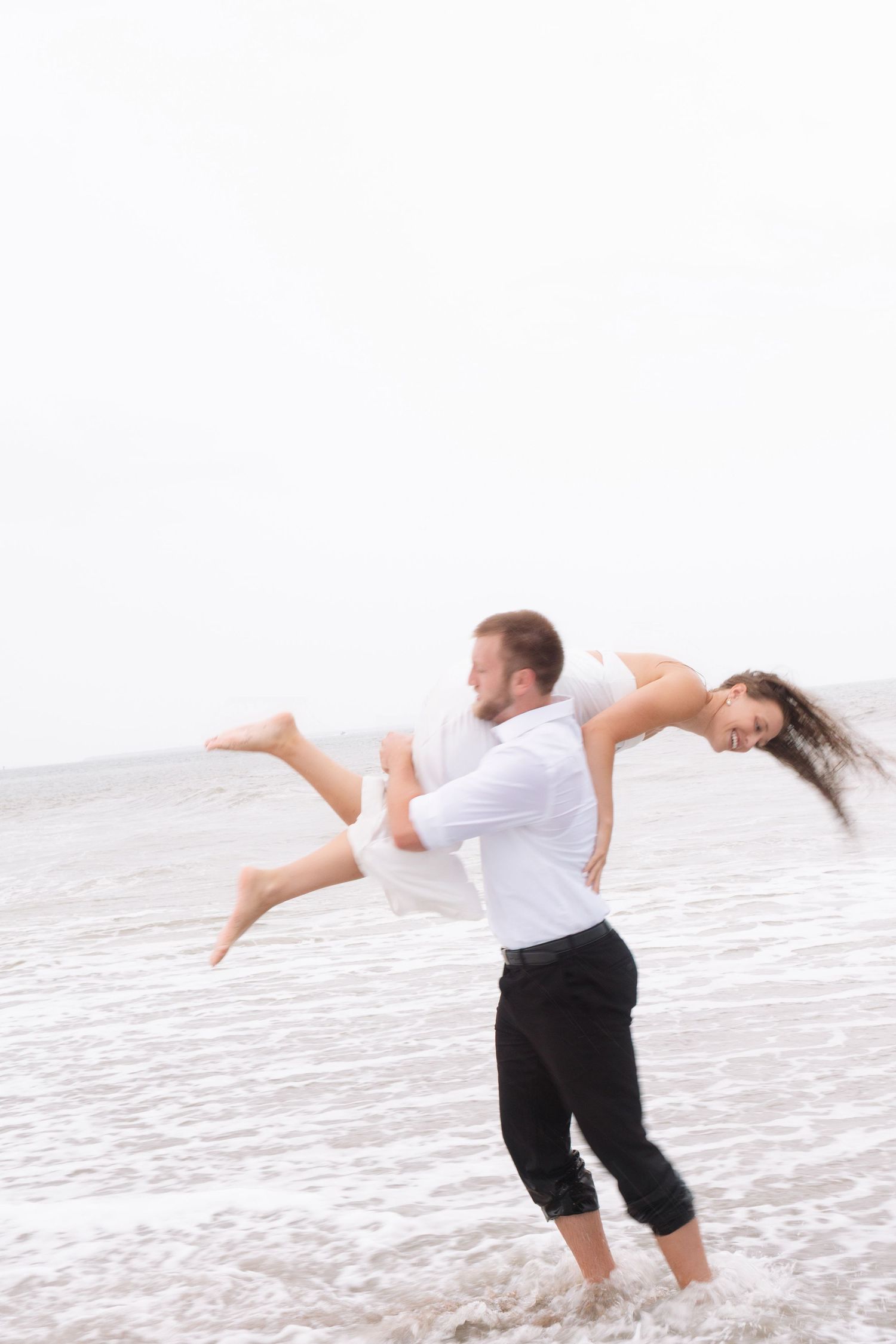 Man lifting woman playfully in ocean waves during a fun beach photo session.