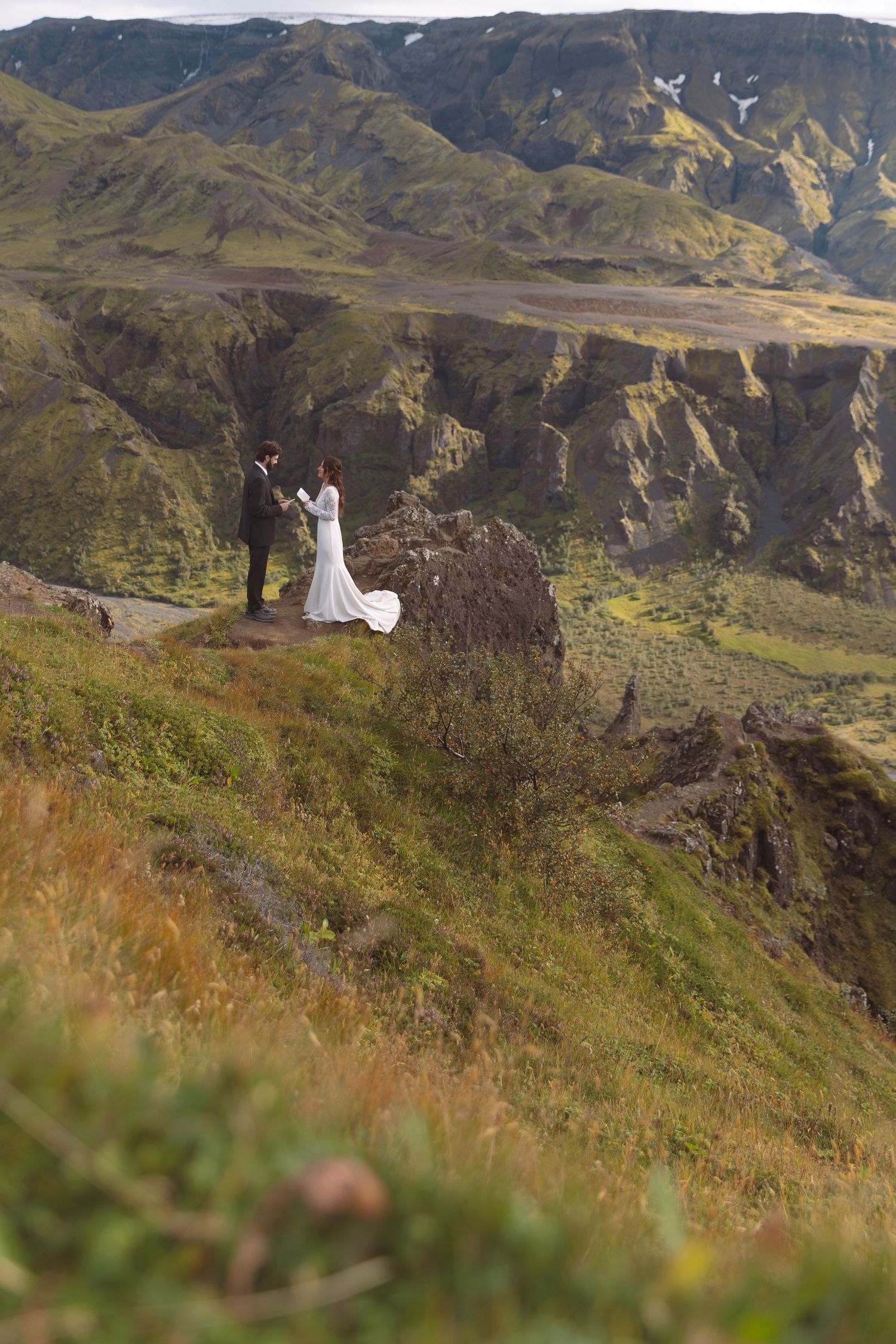 Bride and groom stand on a dramatic Iceland mountain cliff edge during their outdoor elopement ceremony.