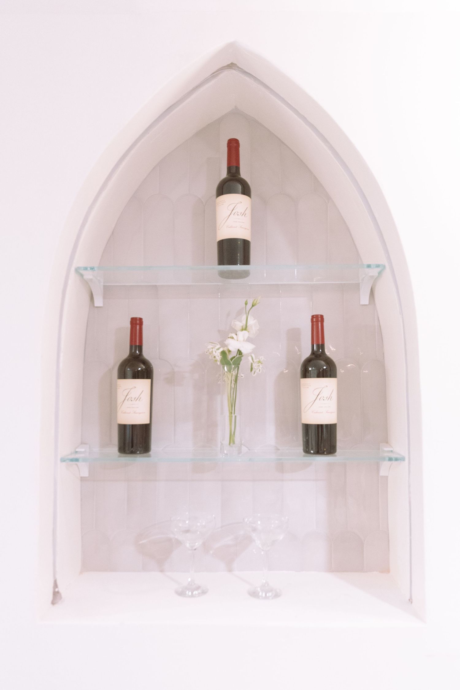 Gothic arch niche display with red wine bottles, white flowers, and martini glasses.