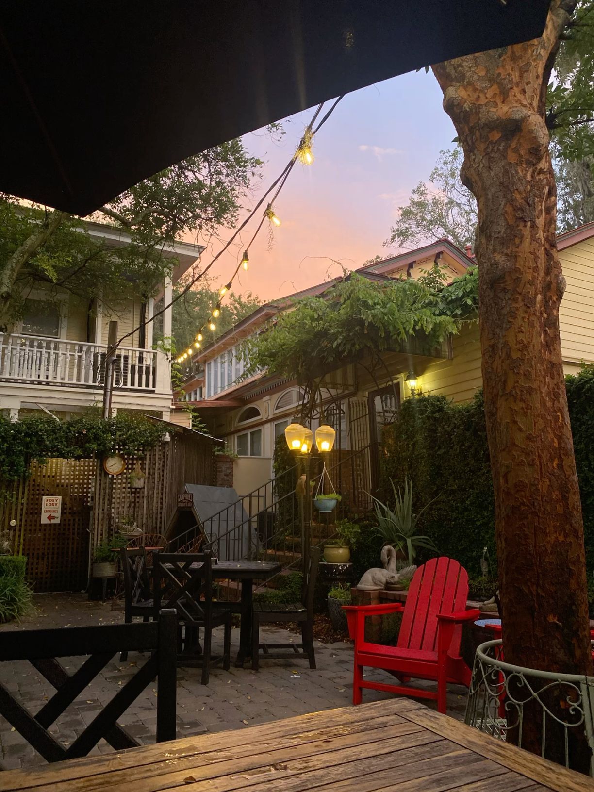 Charming outdoor patio with string lights, red Adirondack chair, and pink sunset sky.