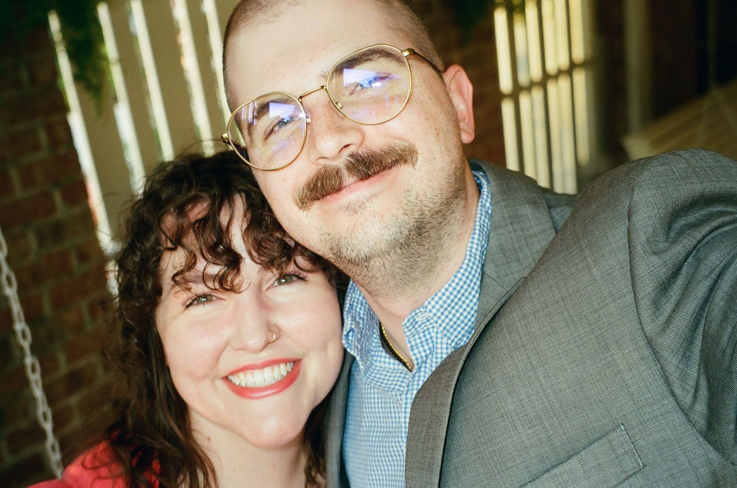 Smiling couple poses closely together, man wearing glasses and suit, woman in red top.