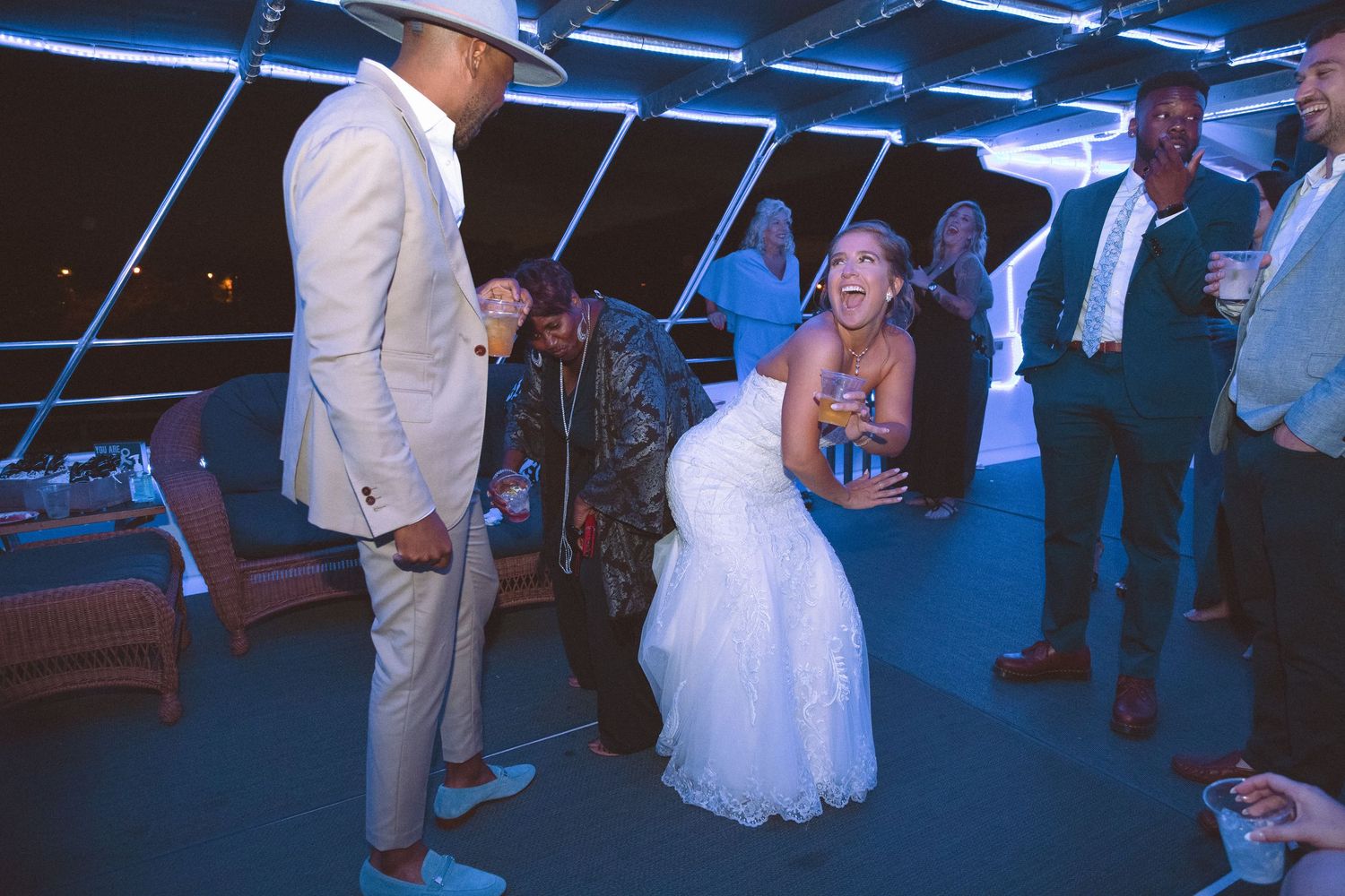 Bride laughing joyfully with wedding guests at a reception venue with blue ambient lighting.