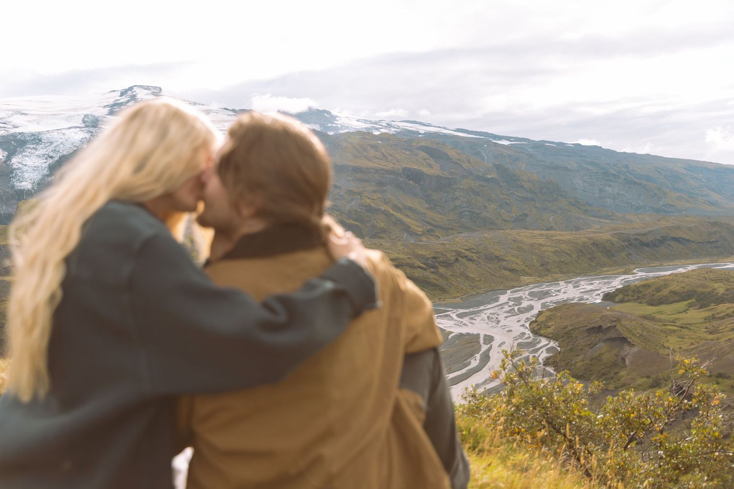 Couple kissing with arms around each other overlooking a scenic mountain valley.