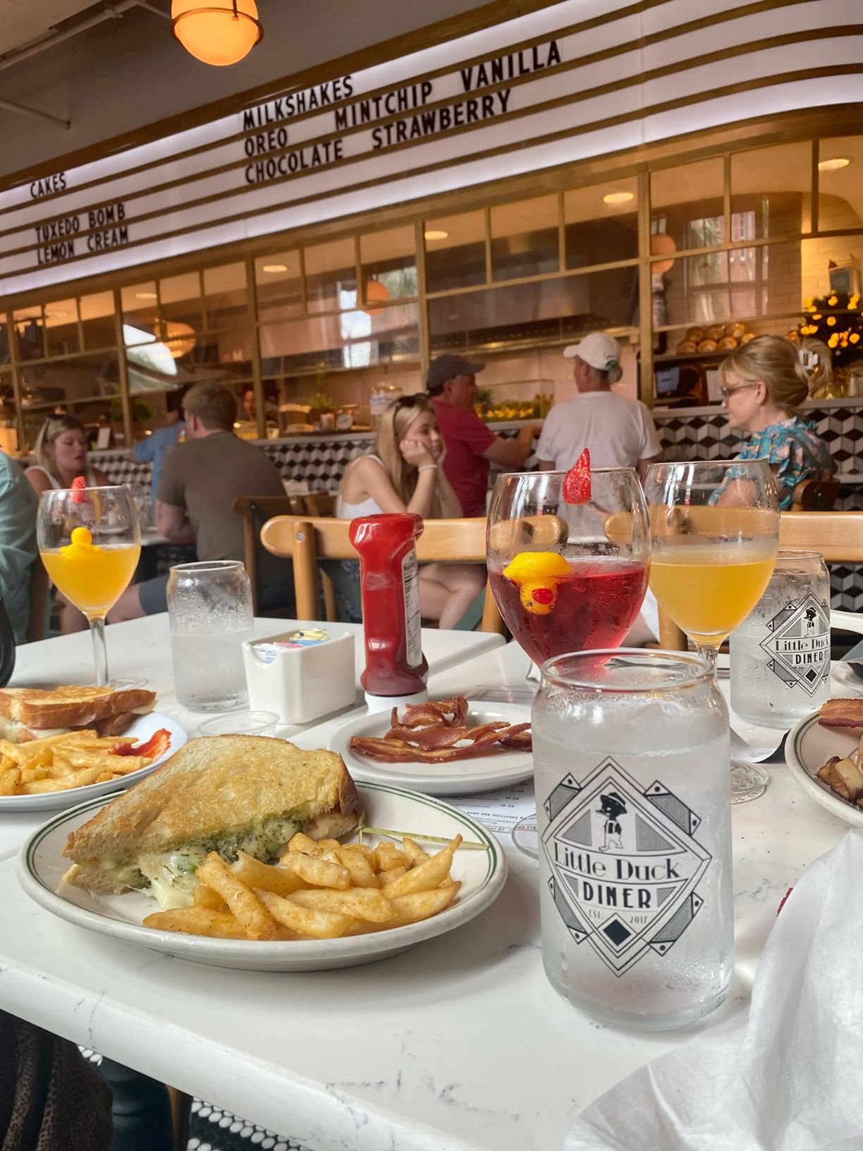 Little Duck Diner brunch spread with sandwiches, mimosas, and sangria in retro diner setting.