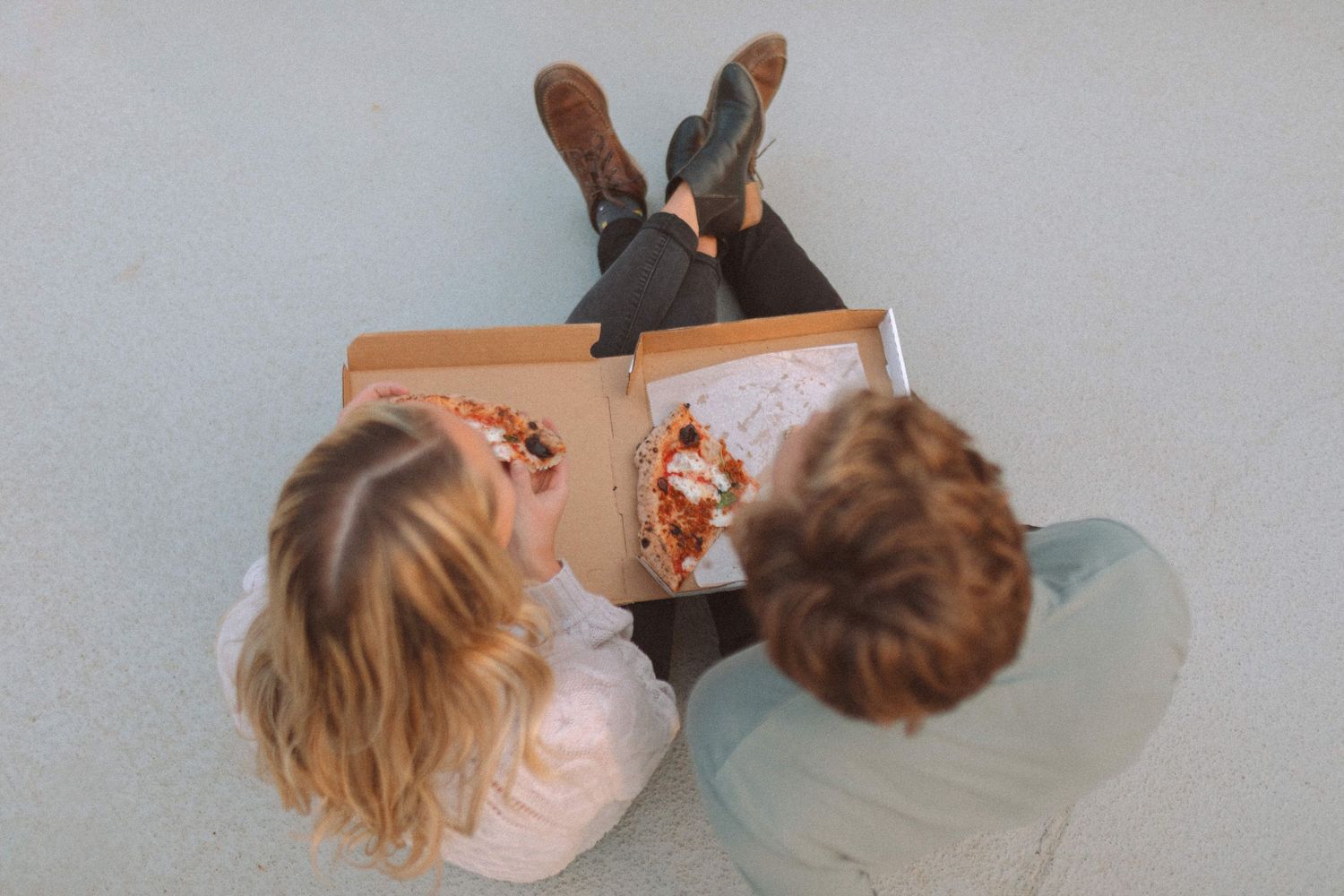 Aerial view of couple sitting on the ground sharing a pizza from an open box.