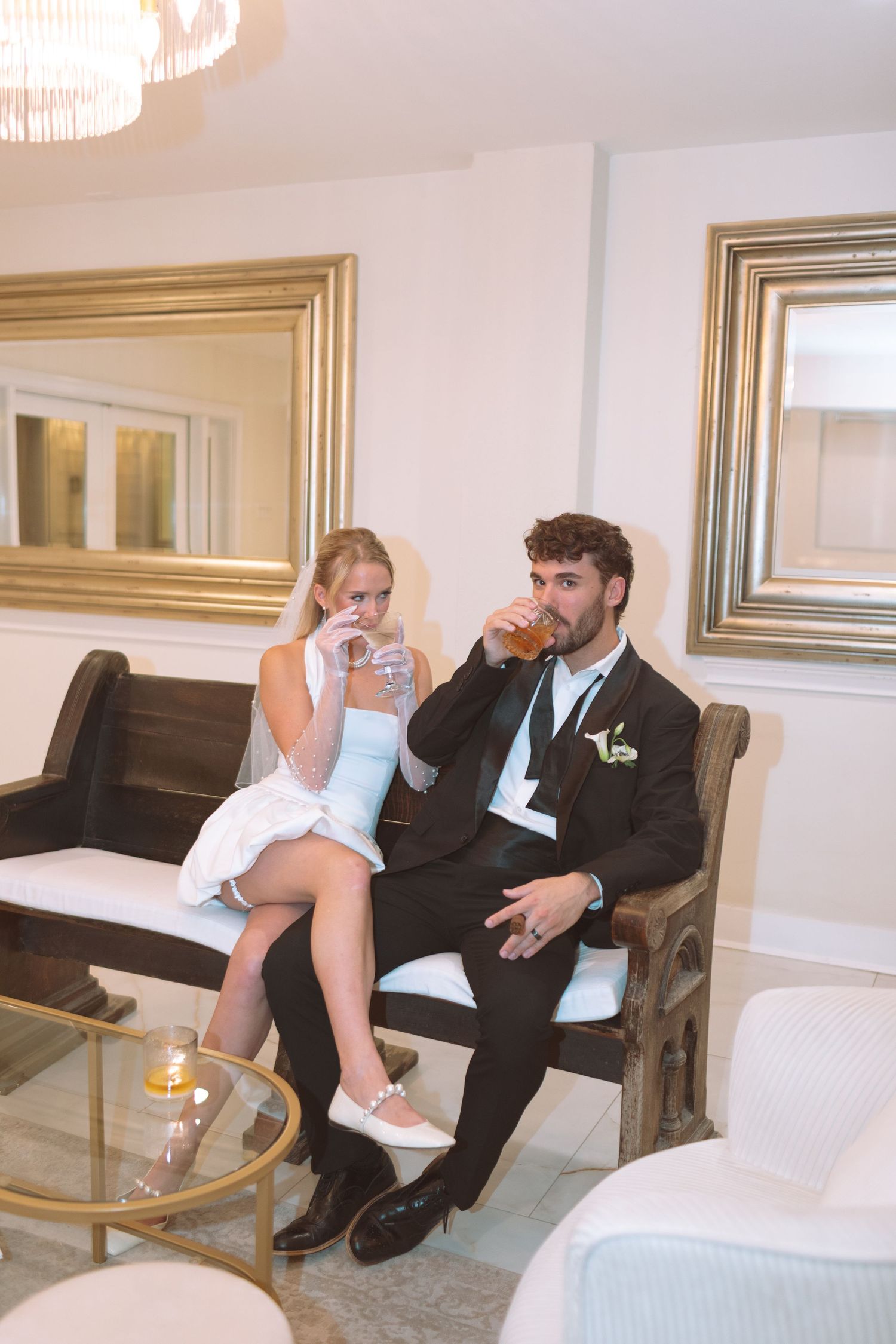 Bride and groom sitting on elegant lounge furniture drinking beverages at their wedding reception.