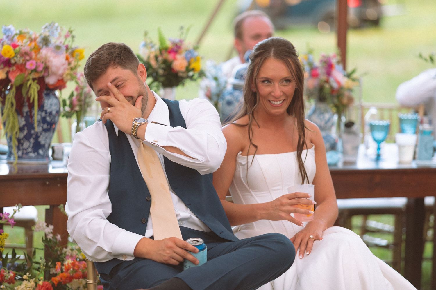 Bride and groom laughing and reacting emotionally during heartfelt wedding reception toasts at sweetheart table.