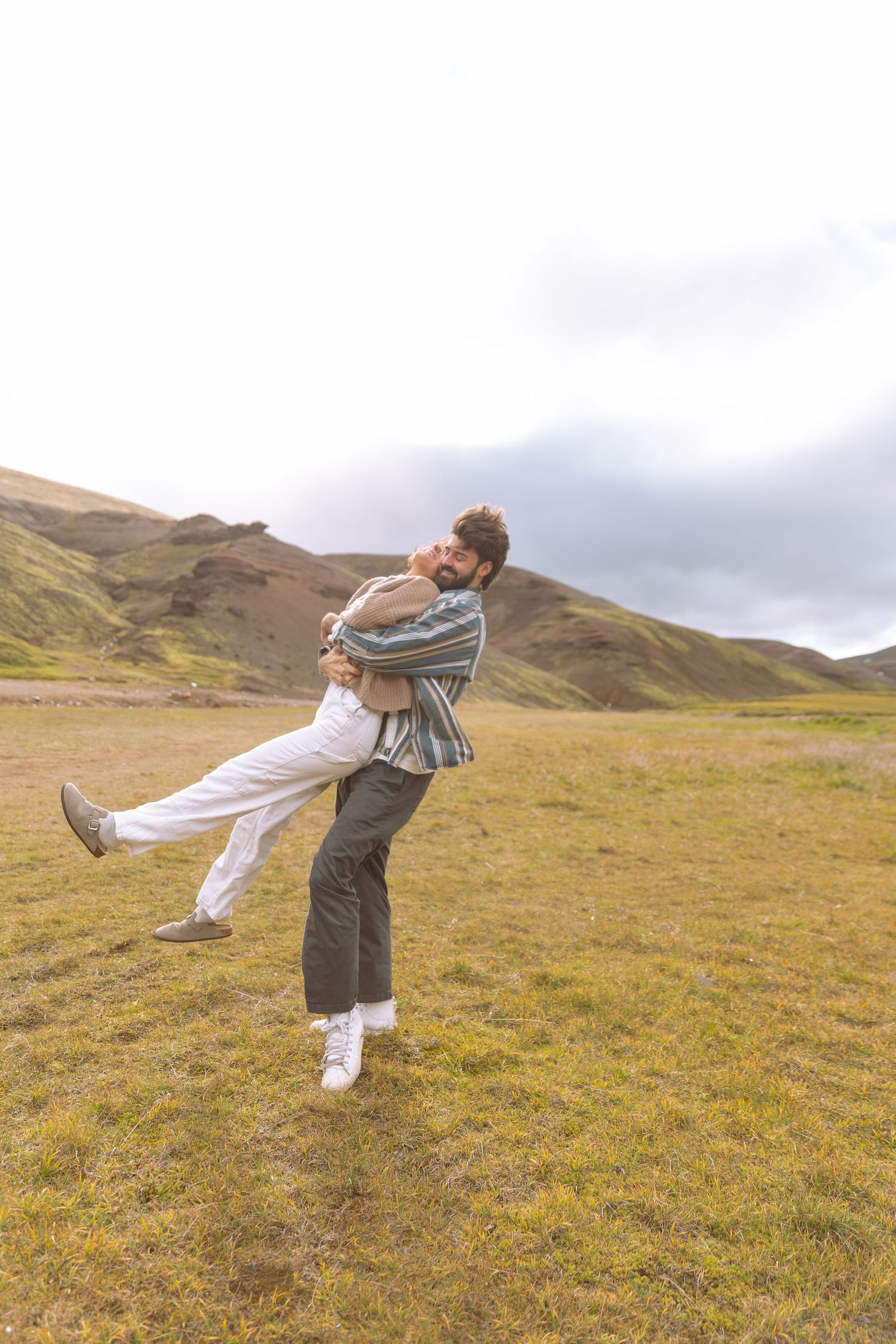 Man spinning woman in his arms in a green highland meadow with mountains in the background.