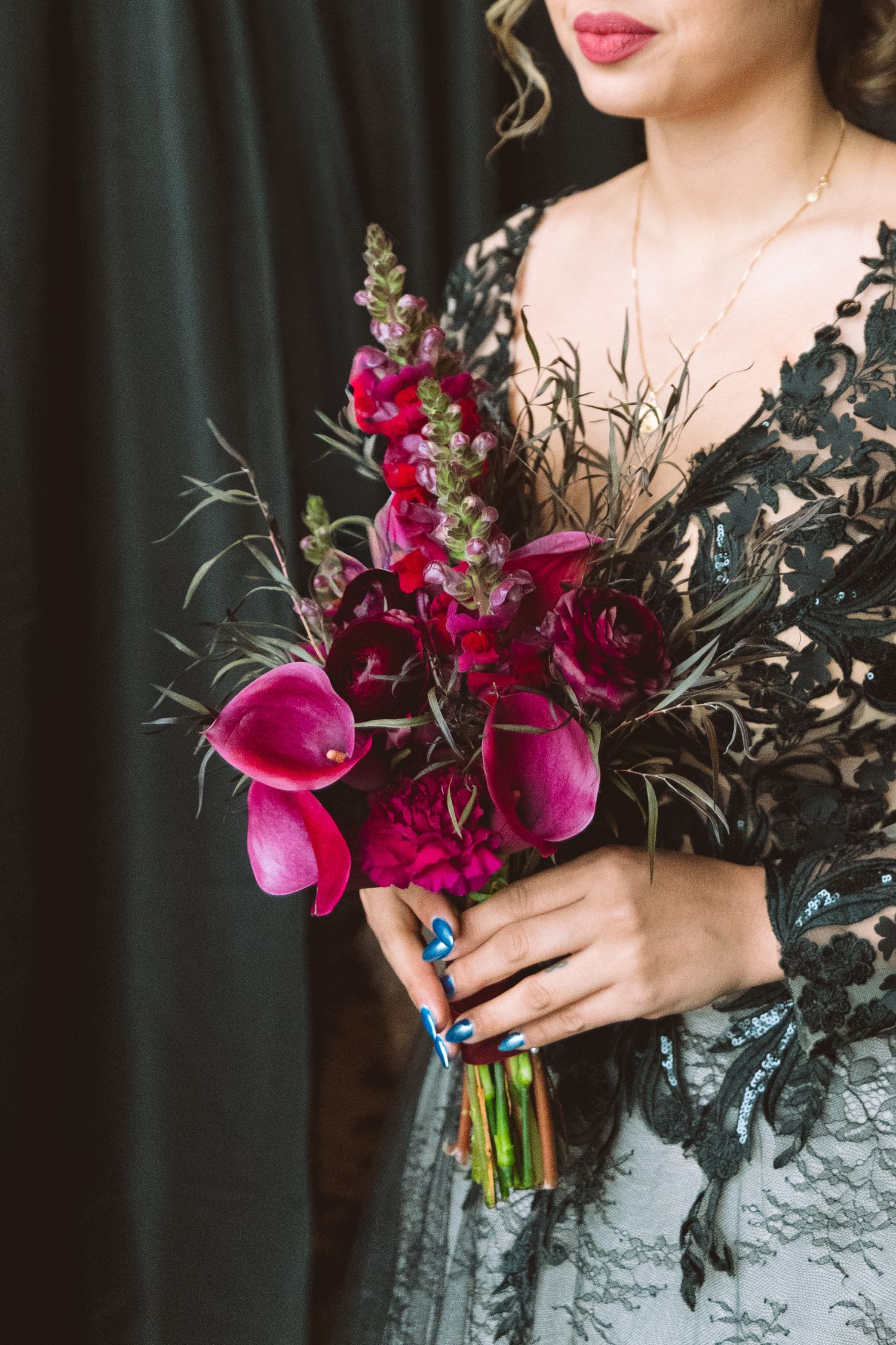 Bride in black lace gown holding a dramatic dark red and magenta bouquet with calla lilies and snapdragons.