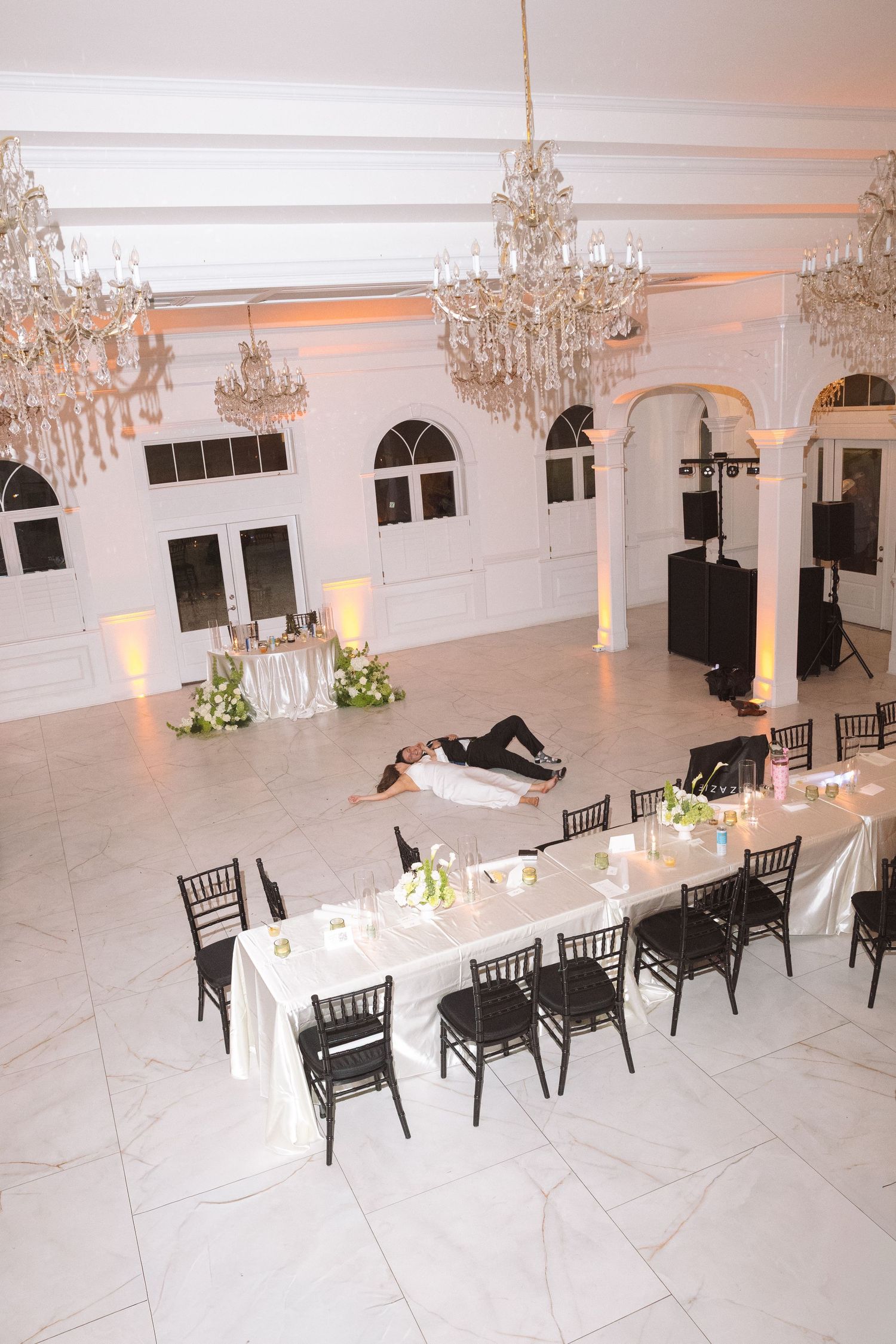 Aerial view of elegant white ballroom reception with crystal chandeliers and marble dance floor.