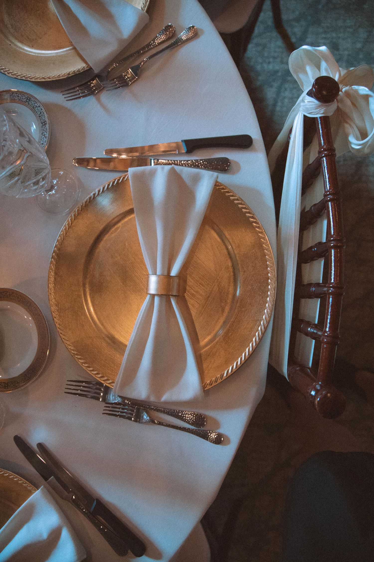 Elegant gold charger plate with white bow-tied napkin and silverware at formal wedding reception.