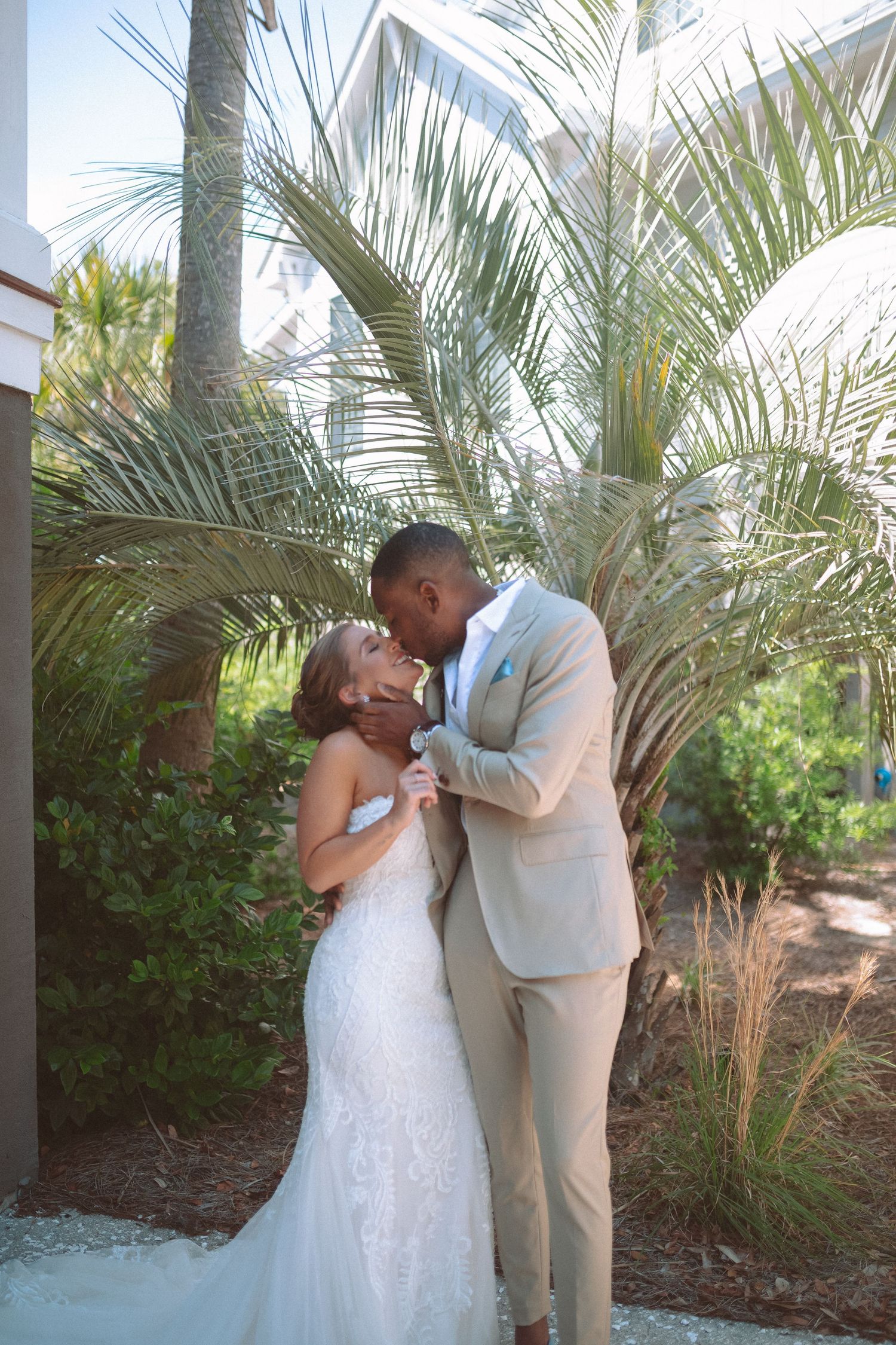 Bride and groom lean in for a kiss during romantic first look surrounded by lush tropical palm trees.