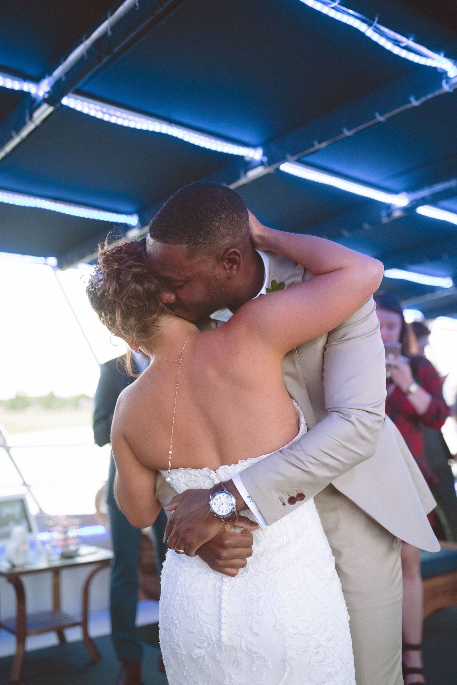 Bride and groom sharing an intimate first dance embrace on a boat wedding reception under blue lights.