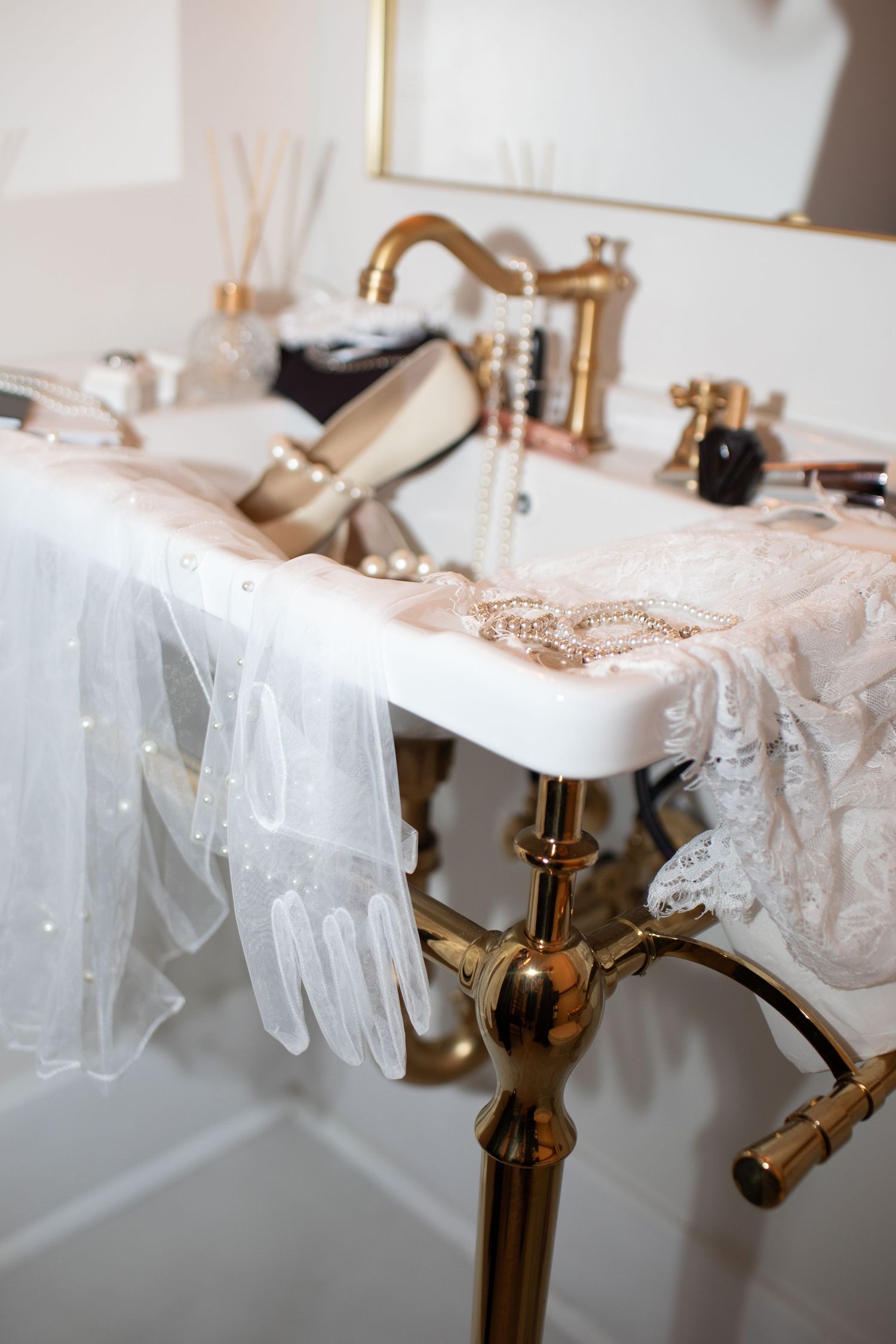 Bridal accessories flat lay with pearl jewelry, lace gloves, heels and veil on gold vintage bathroom vanity.