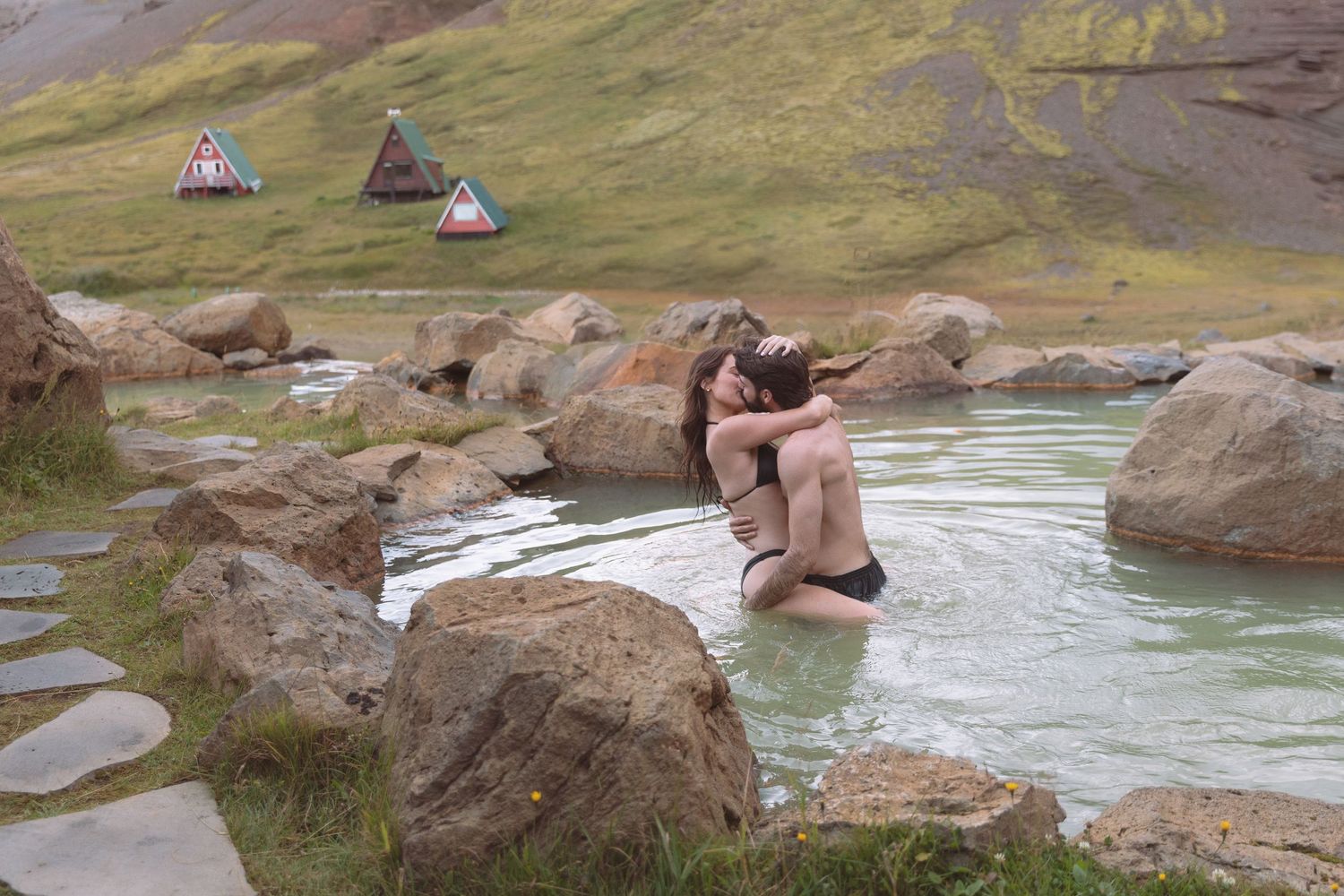 Couple kissing intimately in a natural geothermal pool surrounded by rocks in Iceland.
