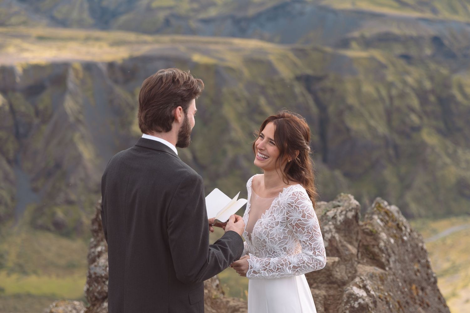 Bride laughs joyfully as groom reads wedding vows during intimate Iceland mountain elopement ceremony.