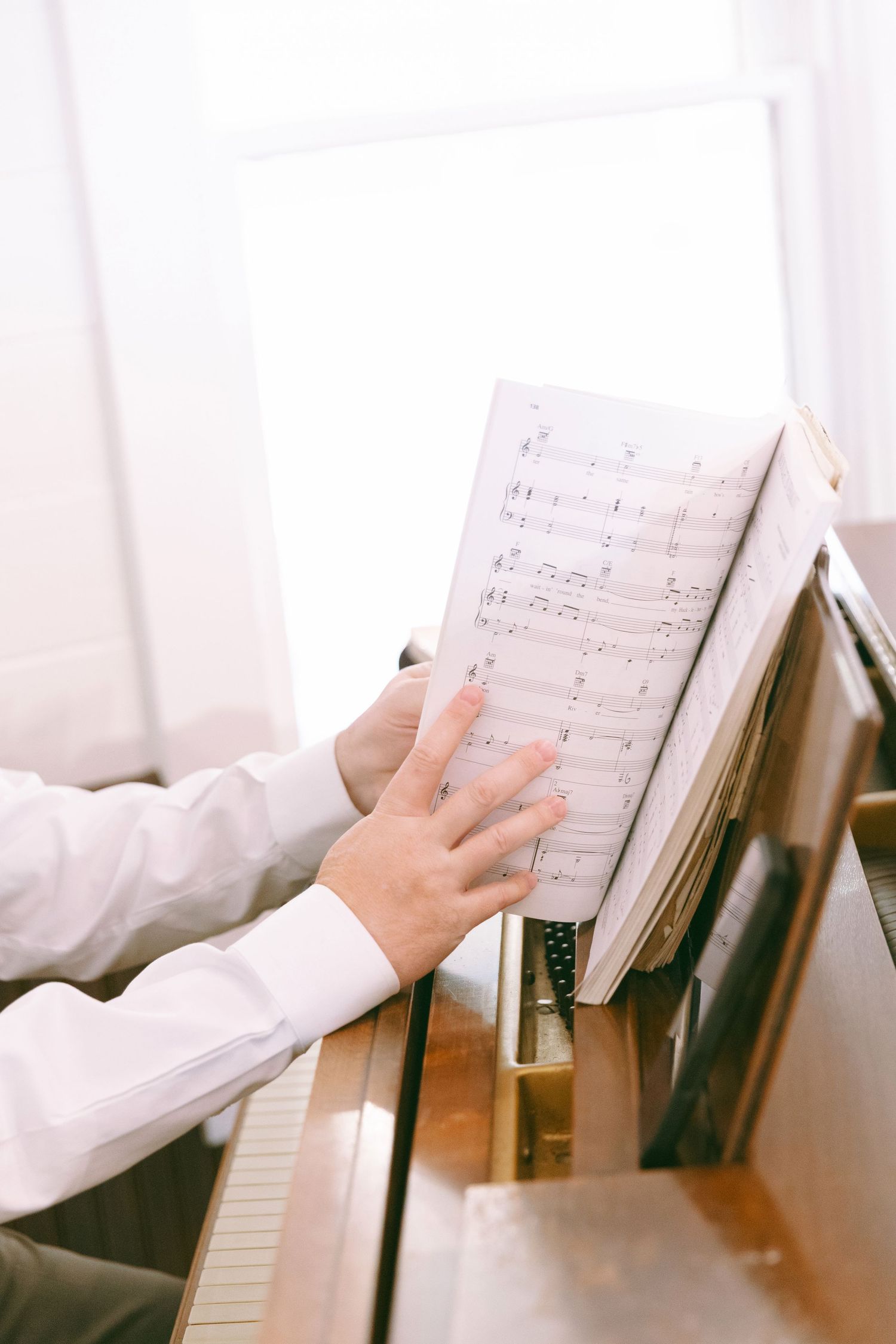 Pianist in white shirt playing piano while reading sheet music on a wooden upright piano.