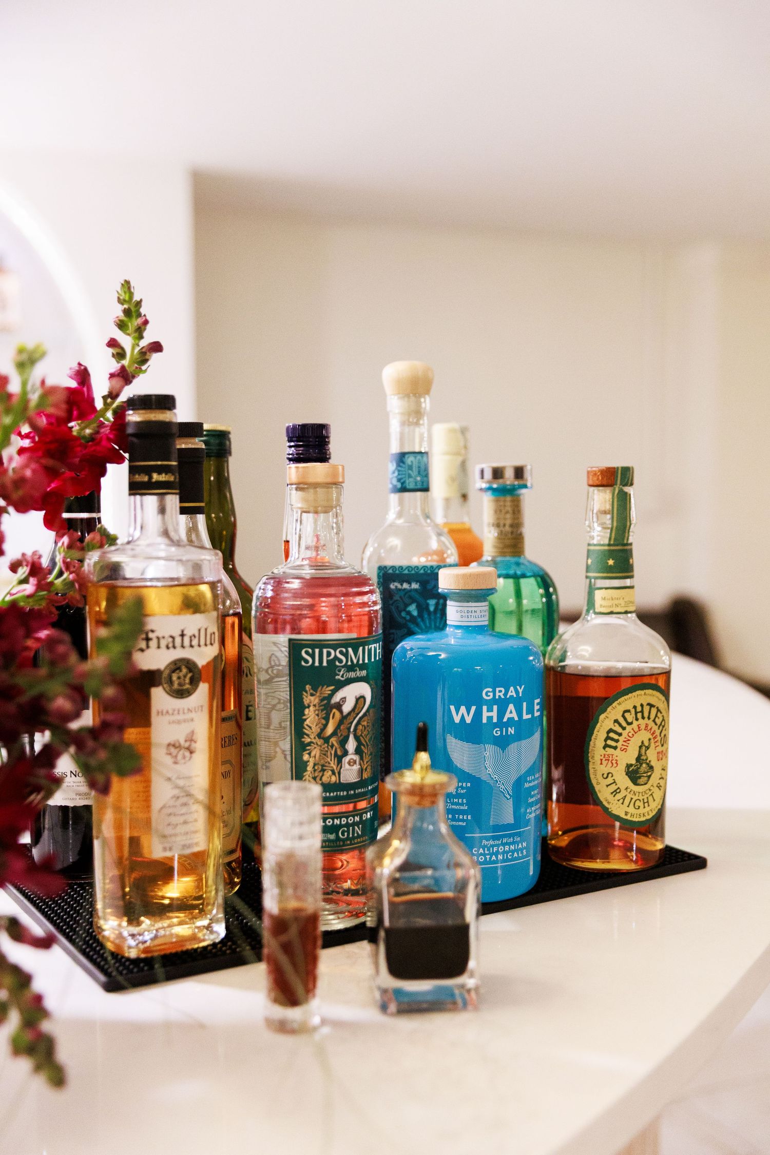 Assorted liquor bottles including Sipsmith gin and Gray Whale gin displayed on a bar counter with floral decor.