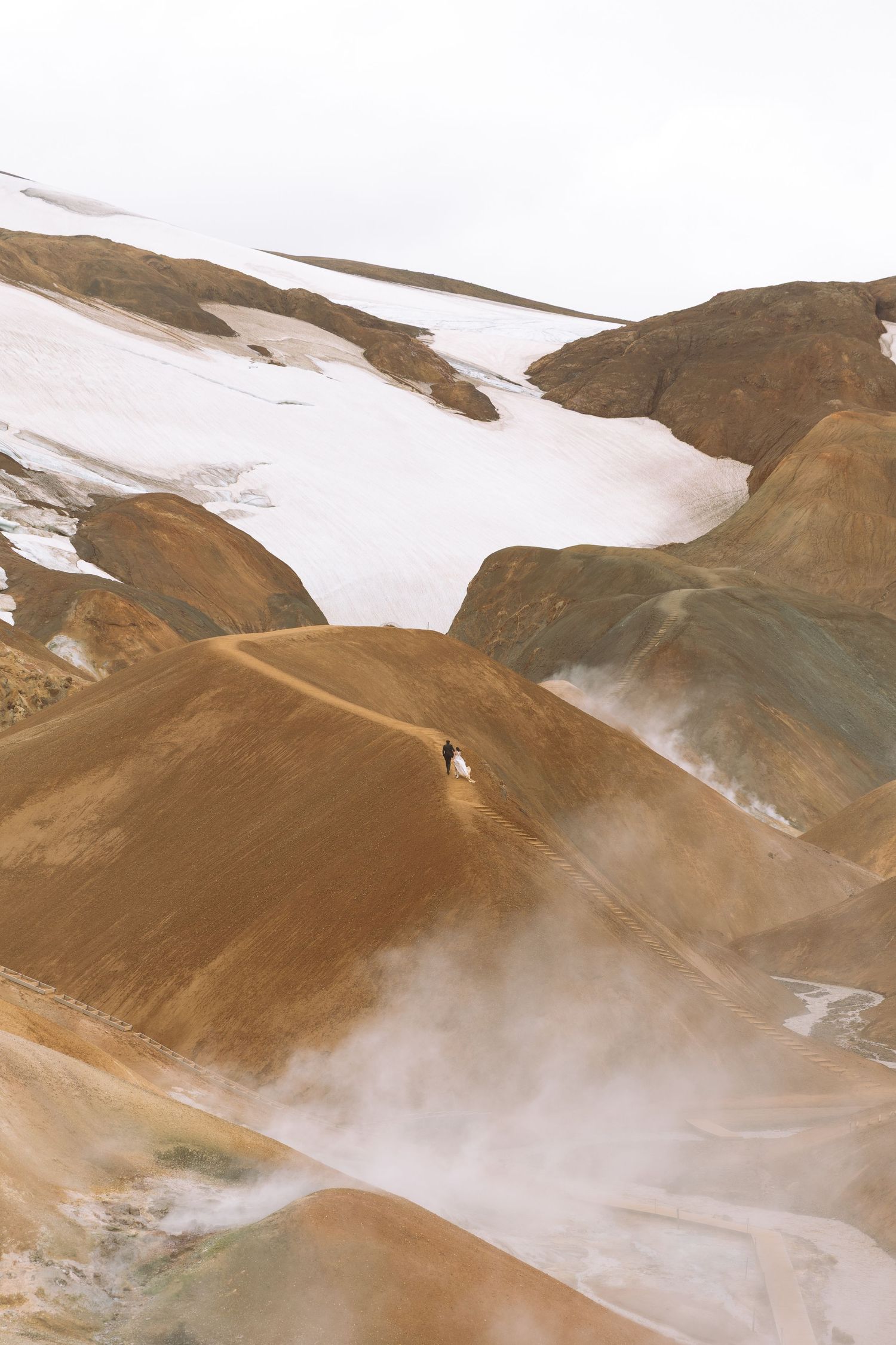 Aerial view of a lone figure on colorful geothermal rhyolite mountains with snow patches in Iceland.