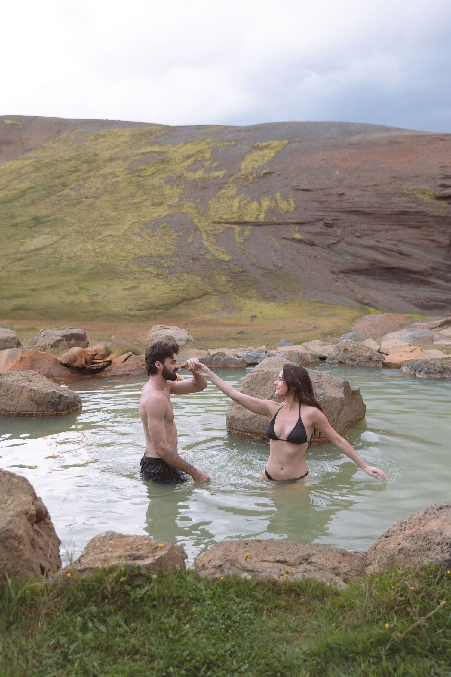 Couple holding hands and playing in a natural geothermal pool in Iceland.