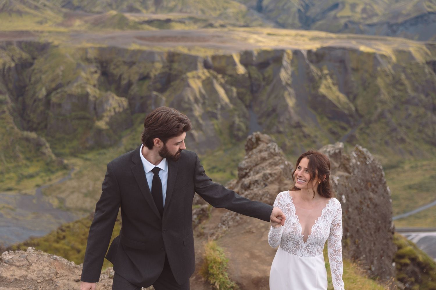 Bride and groom hold hands on a dramatic Iceland mountain landscape during their outdoor wedding photo shoot.