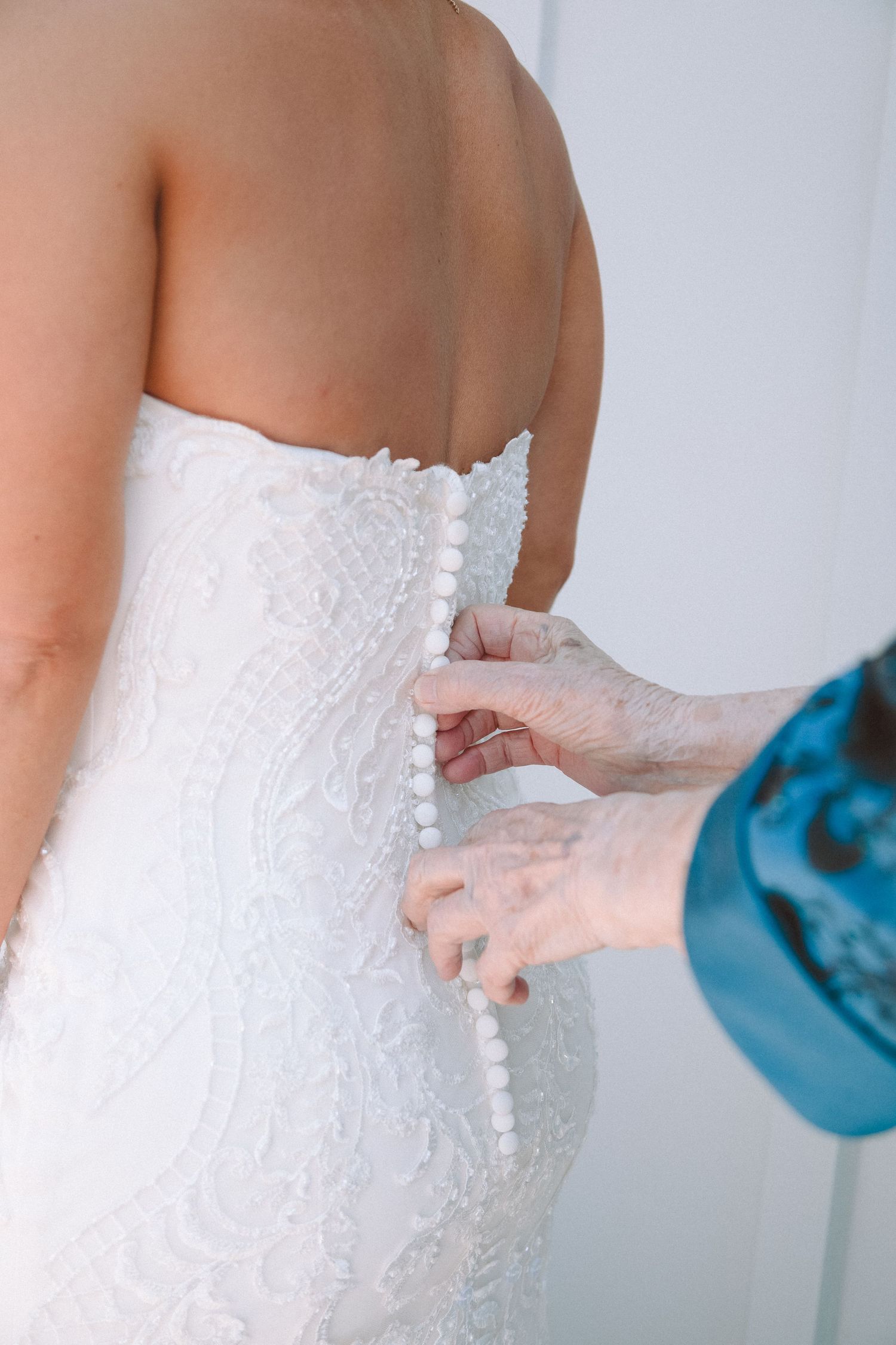 Close-up of pearl buttons being fastened on the back of a white lace bridal gown.
