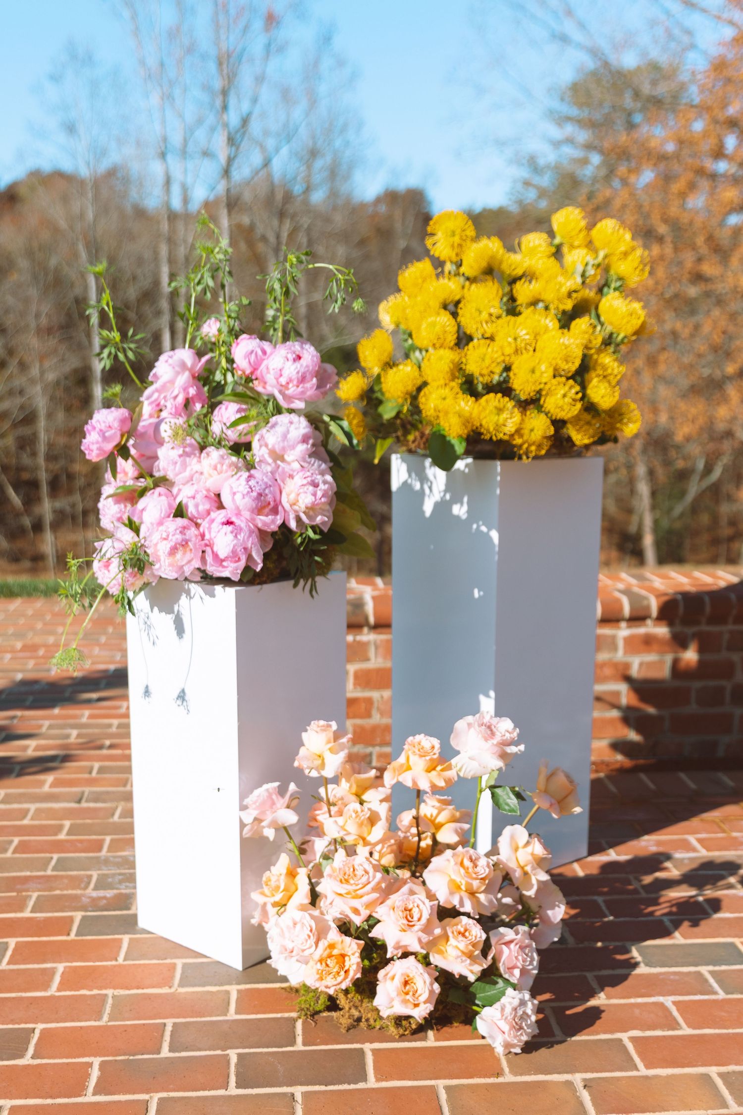 Colorful pink, yellow, and peach floral arrangements on white pedestals outdoors.