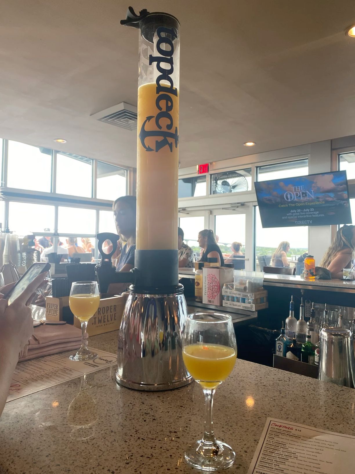 Tall Topdeck beer tower with two glasses of orange juice at a bright bar.