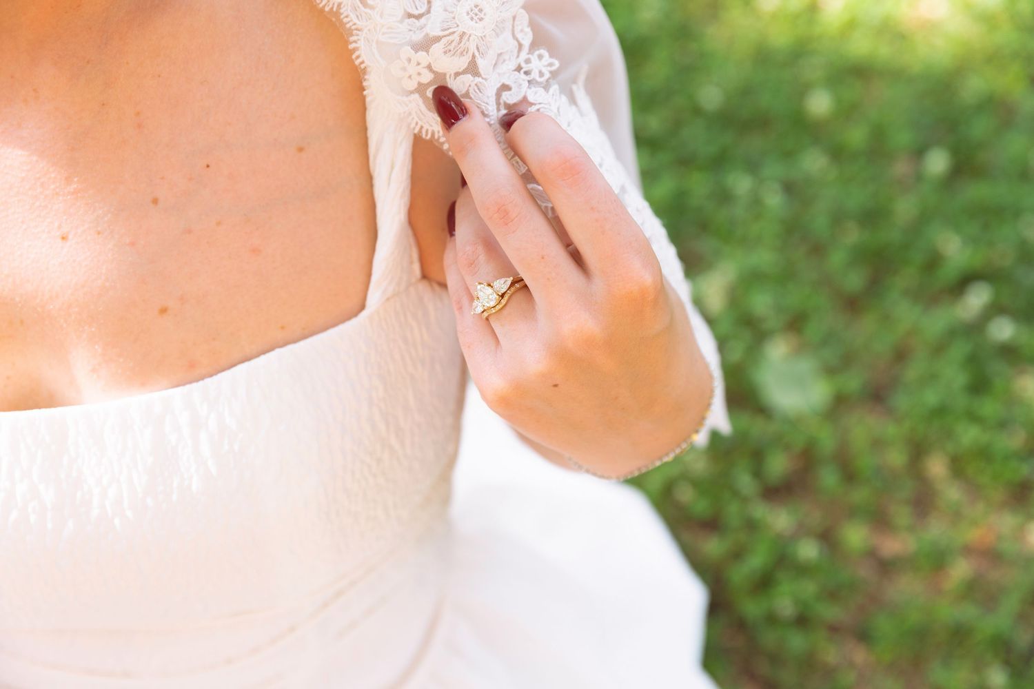 Detail shot of bride's hand with gold wedding band resting on lace wedding dress outdoors.