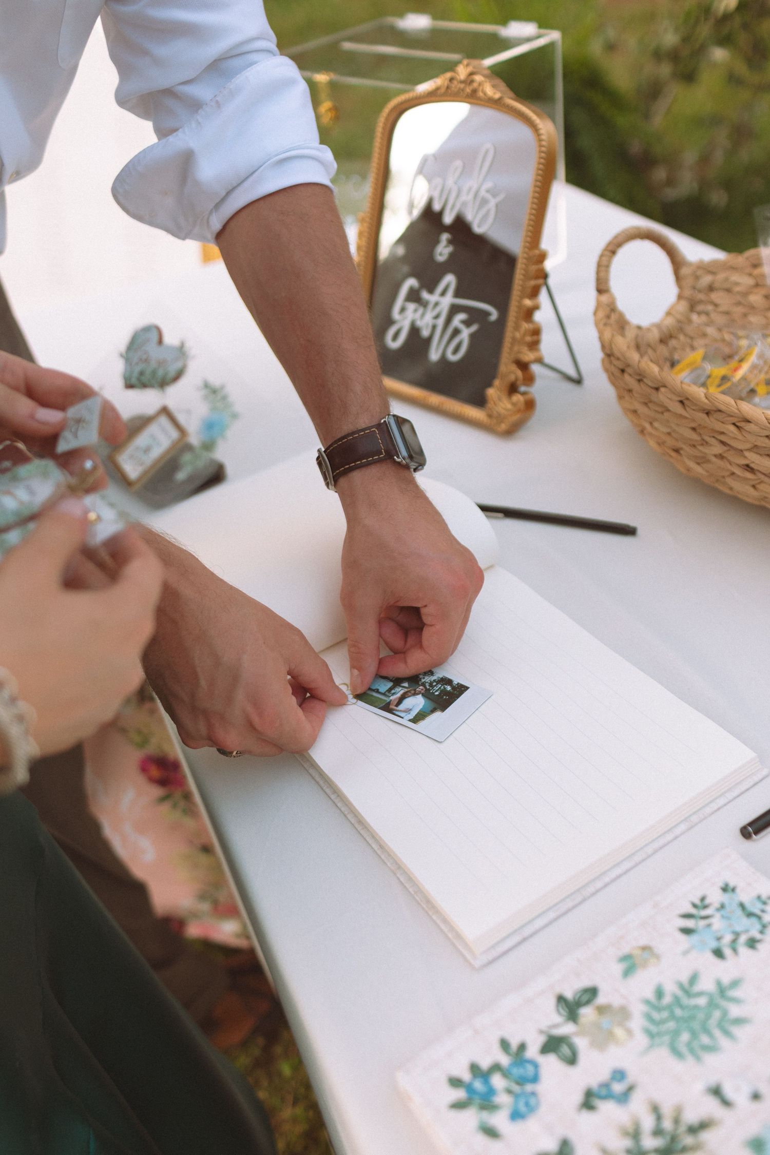 Groom placing a Polaroid photo into a wedding guest book at a decorated cards and gifts table.