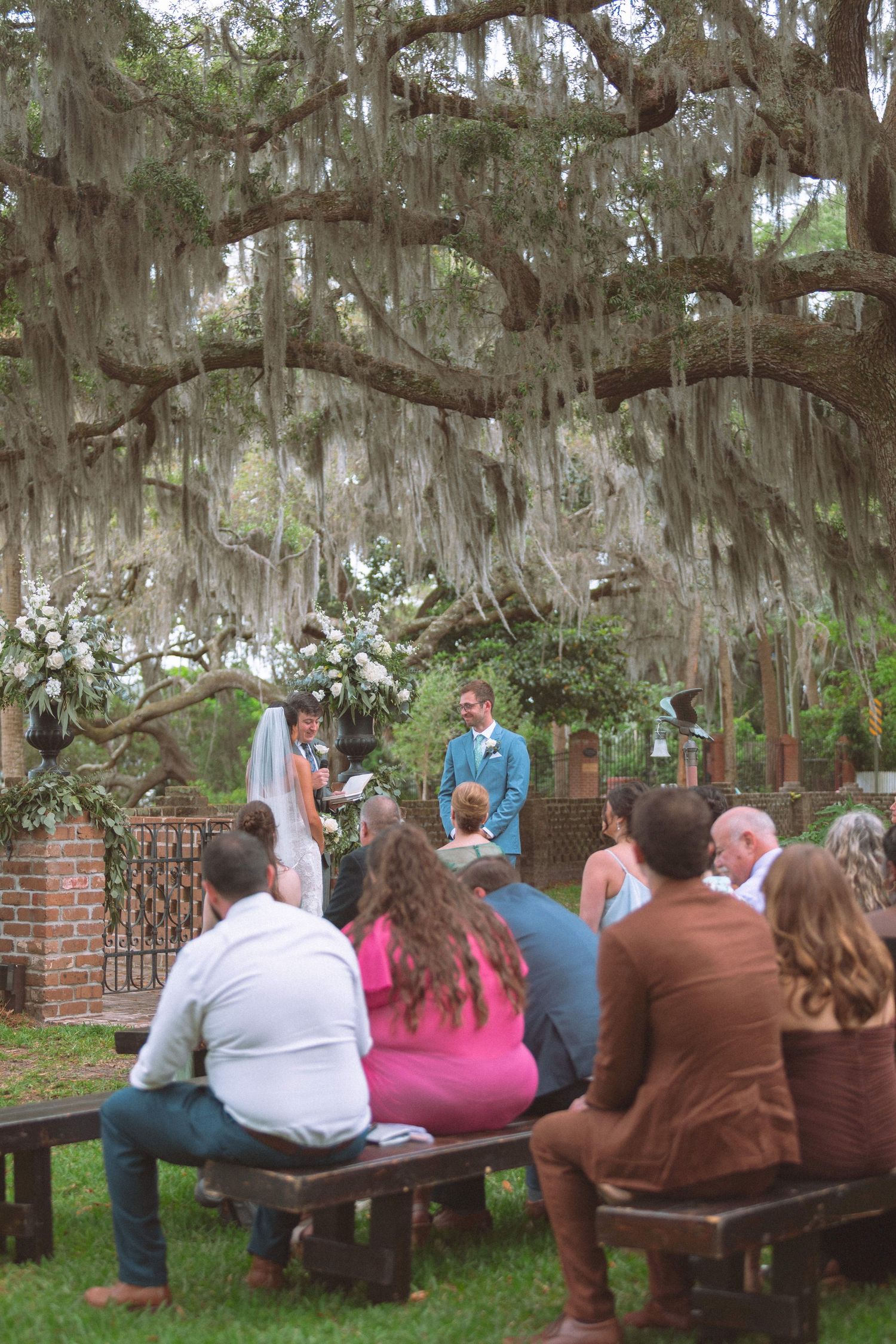 Intimate outdoor wedding ceremony under sprawling oak tree draped with Spanish moss in the South.
