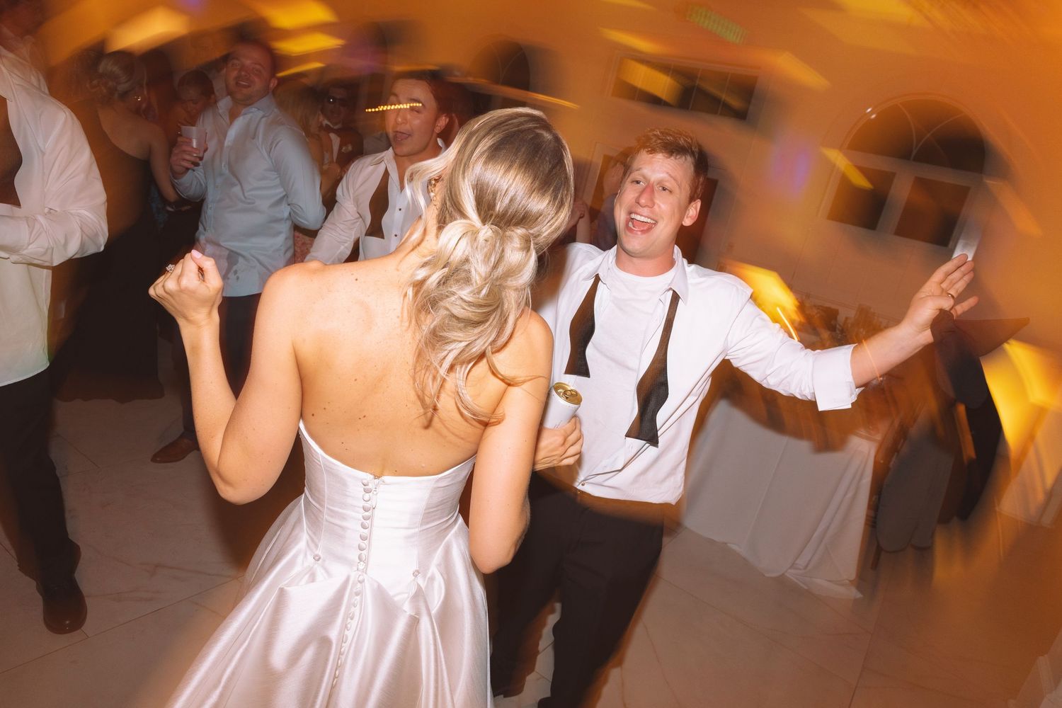 Bride in white strapless gown dancing joyfully with smiling groom in black tie at wedding reception.