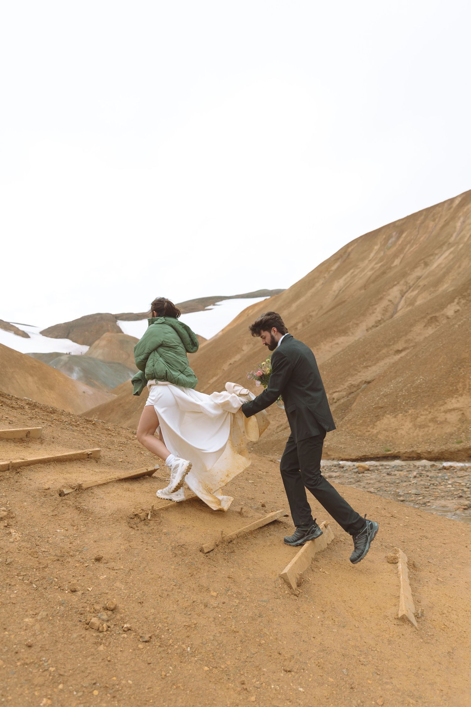 Groom helps bride climb wooden steps up Iceland's volcanic hillside during their outdoor elopement shoot.