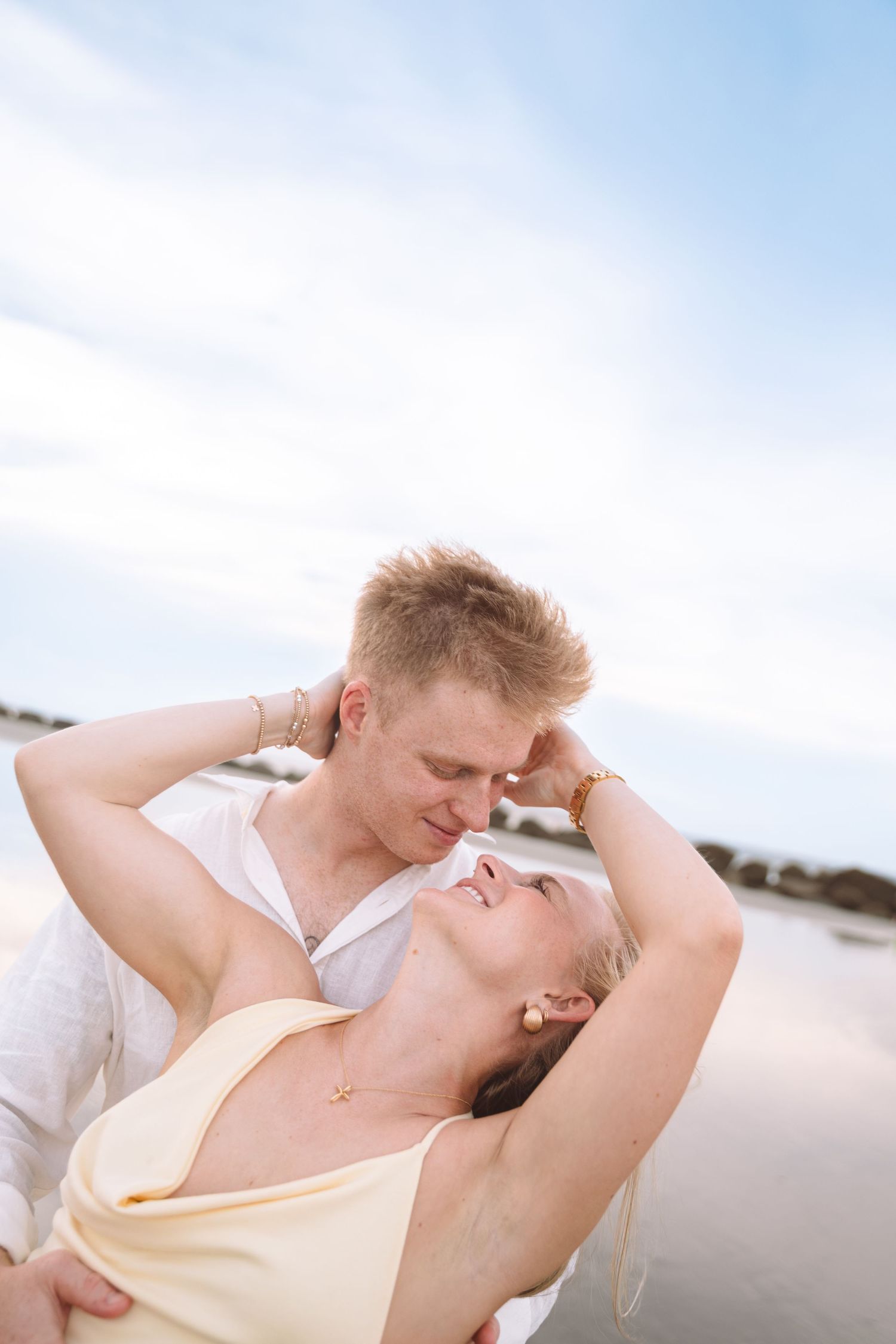 Romantic couple almost kissing on a sunny beach, woman in yellow dress leaning back.