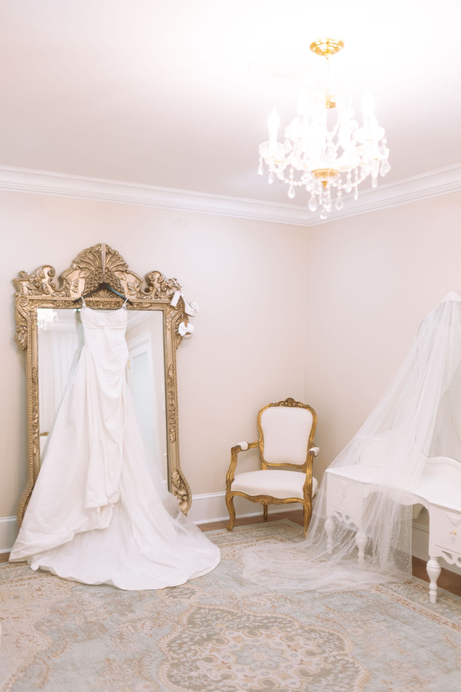 White wedding dress hanging on ornate gold mirror in elegant bridal suite.