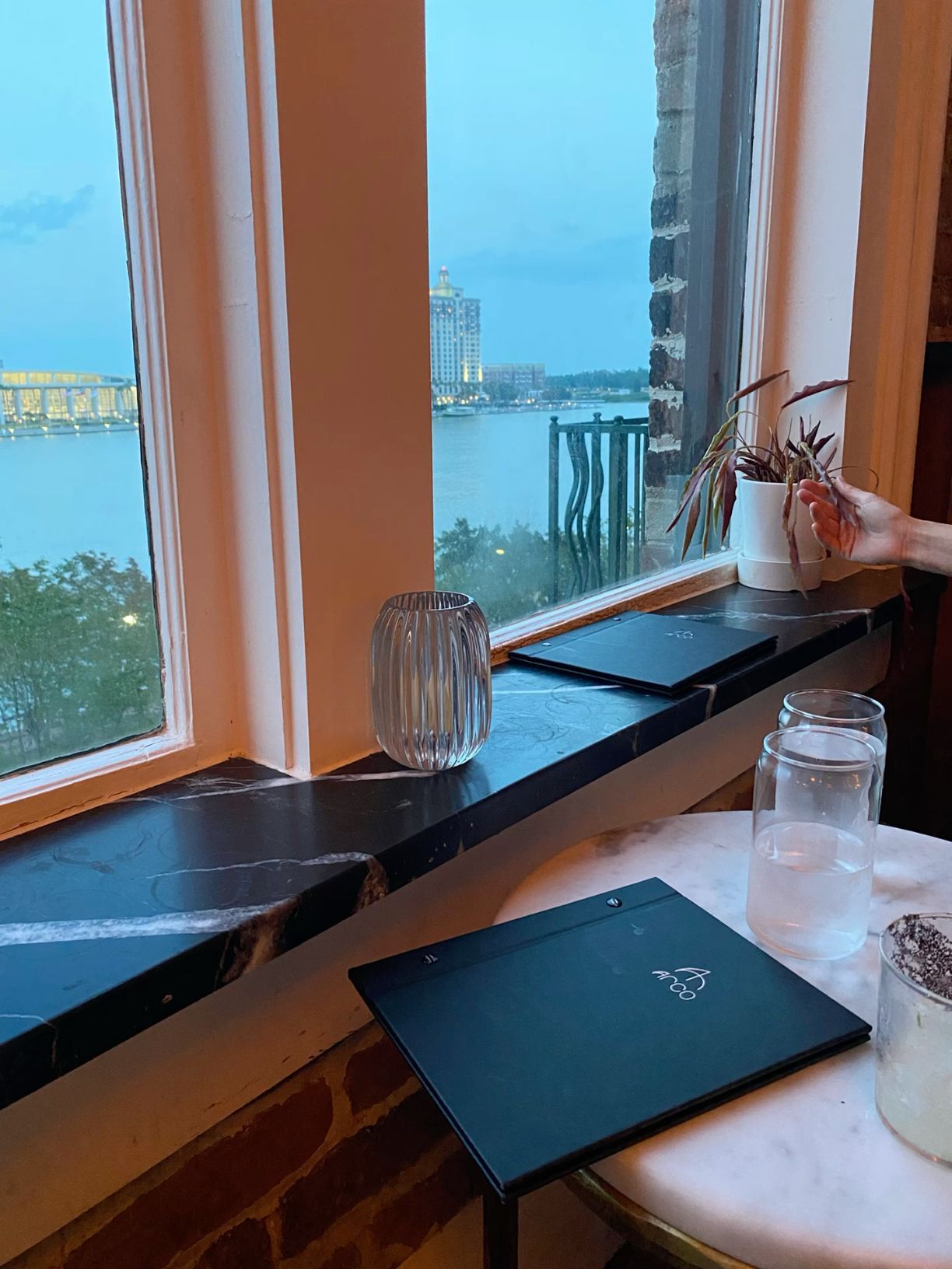 Waterfront restaurant window view at dusk with black marble menu holders and small potted plant.