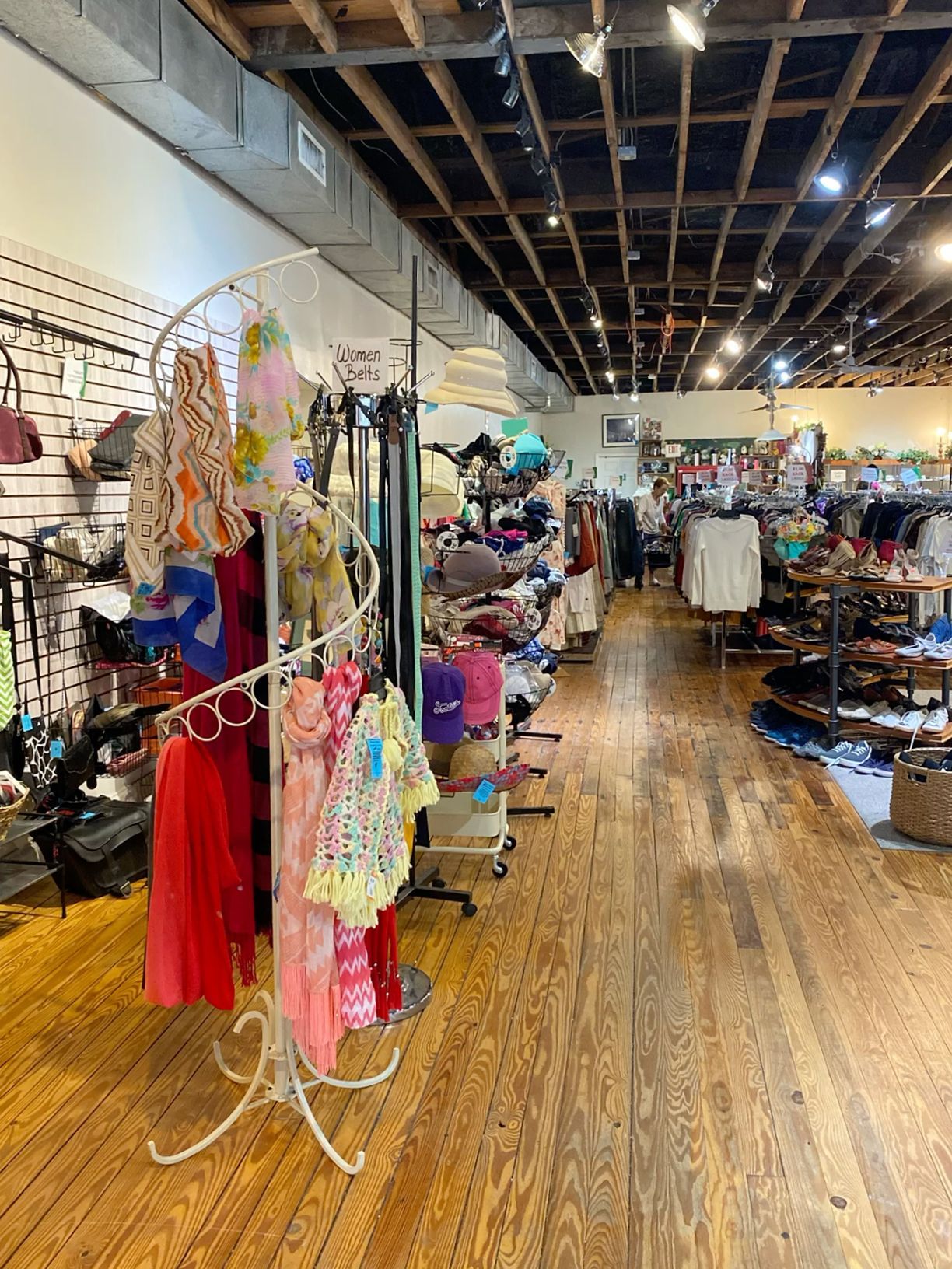 Bright boutique clothing store interior with colorful garments on racks and hardwood floors.