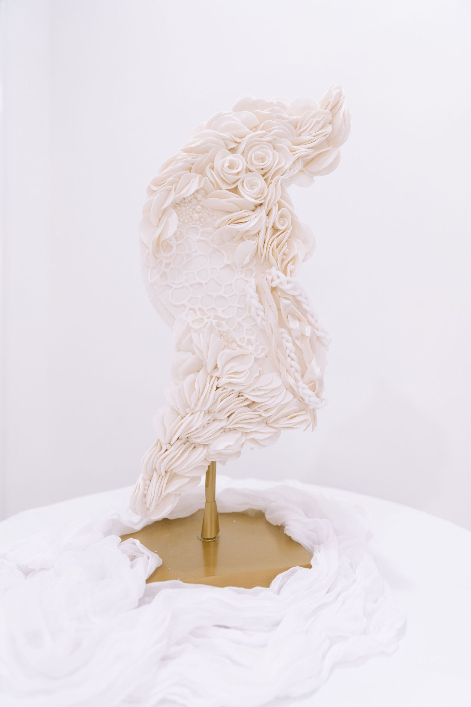 Elegant white wedding cake topper sculpture with intricate floral and feather details on a gold stand.