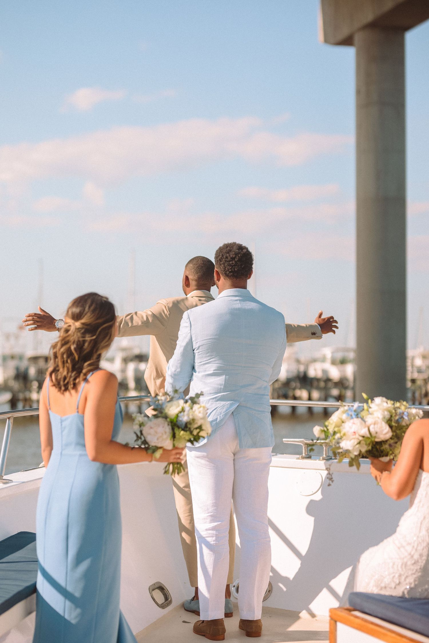 Wedding party celebrating on the deck of a boat overlooking a marina on a sunny day.