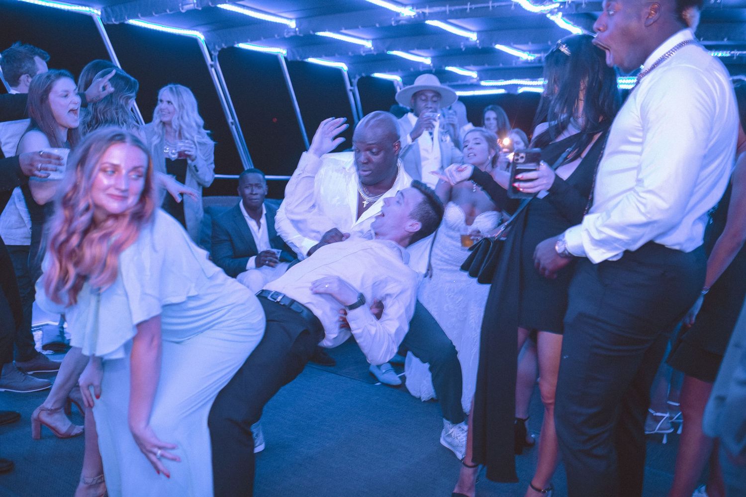 Guests doing the limbo dance at a wedding reception party with blue neon lights.