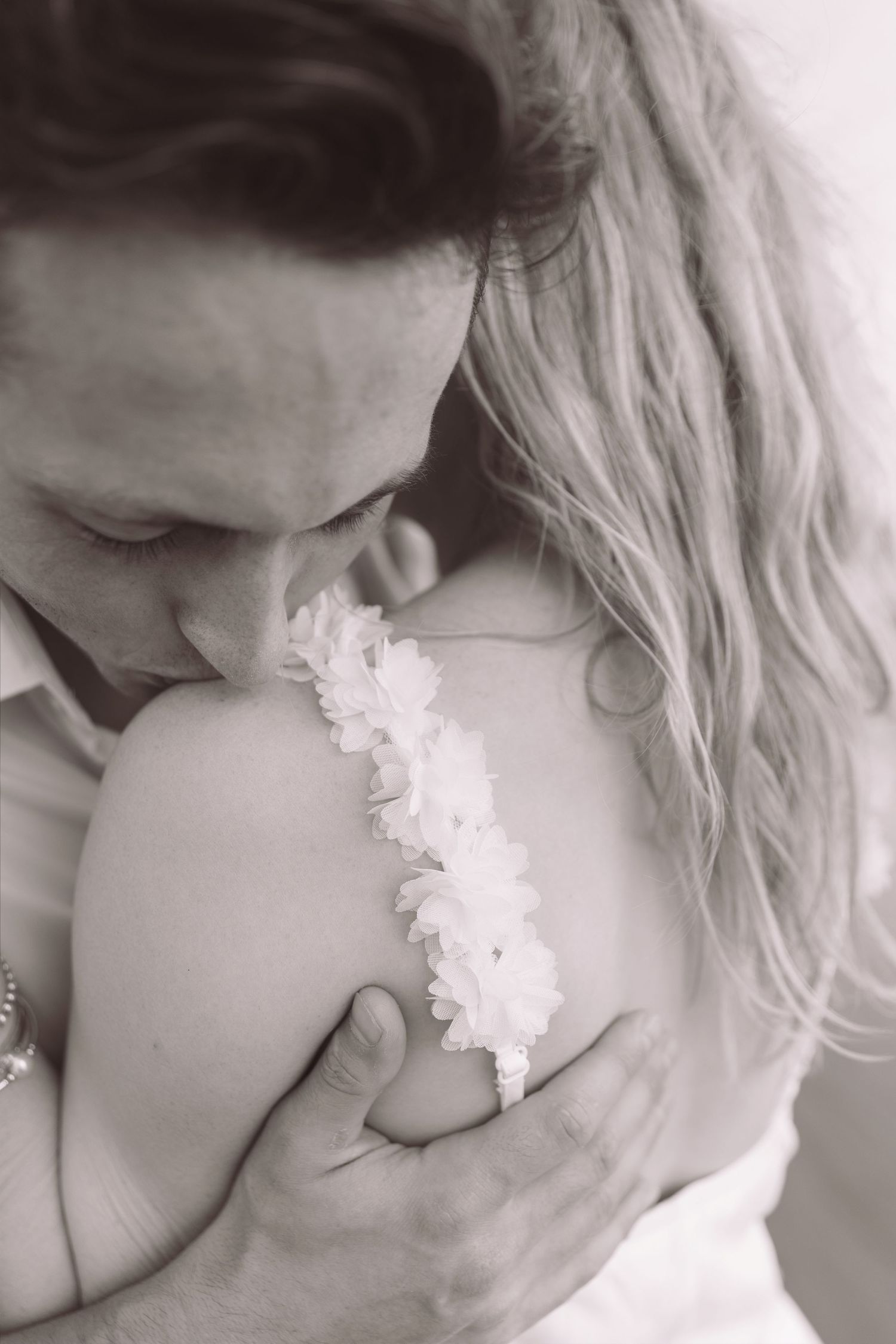 Black and white close-up of groom kissing bride's shoulder tenderly.