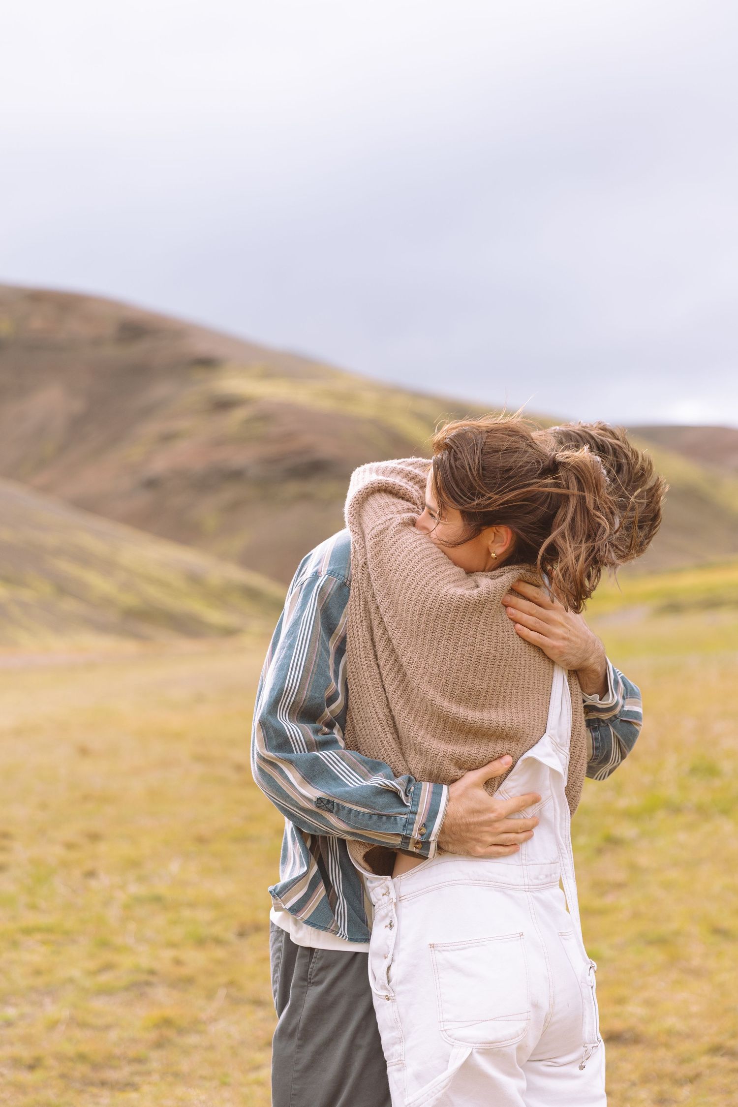 Couple sharing a warm embrace in a vast green hillside landscape outdoors.