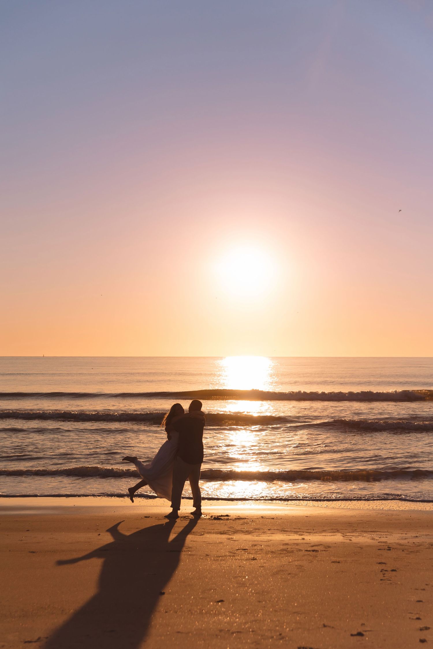 Romantic couple silhouetted against a golden sunset on a sandy beach, waves gently rolling in behind them.
