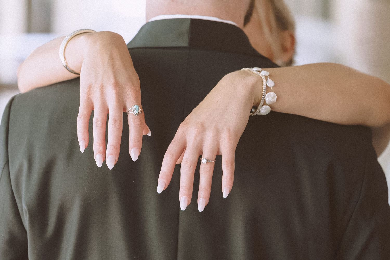 Close-up of bride and groom embracing showing engagement ring, wedding band, and pearl bracelet.